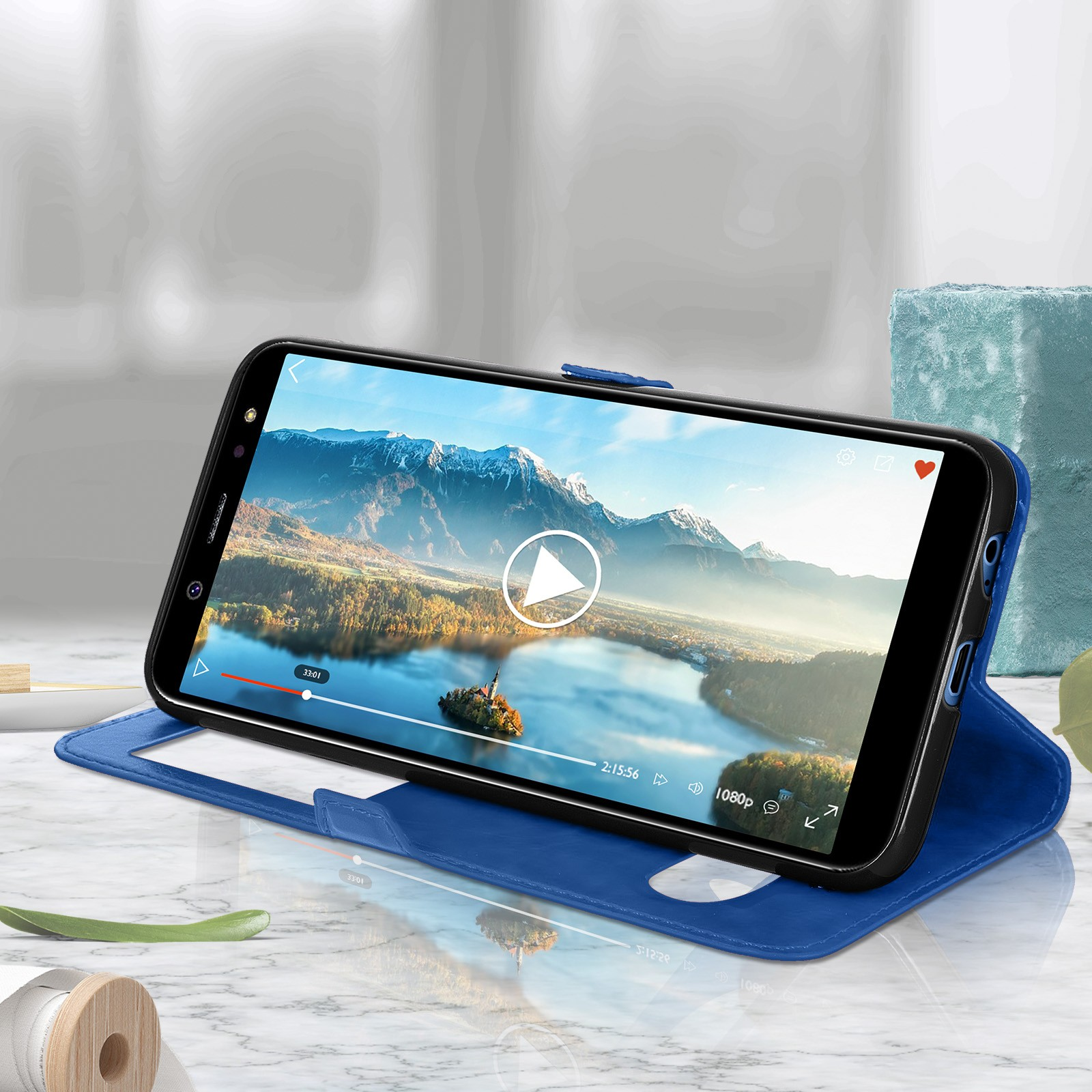 Custodia blu per telefono con un telefono che mostra un video. Una bobina di legno e un vaso sono nella scena.