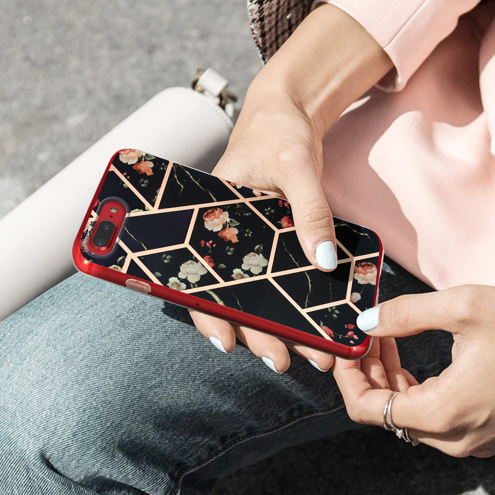 Le mani di una donna che tiene un telefono con una custodia nera a fantasia floreale.