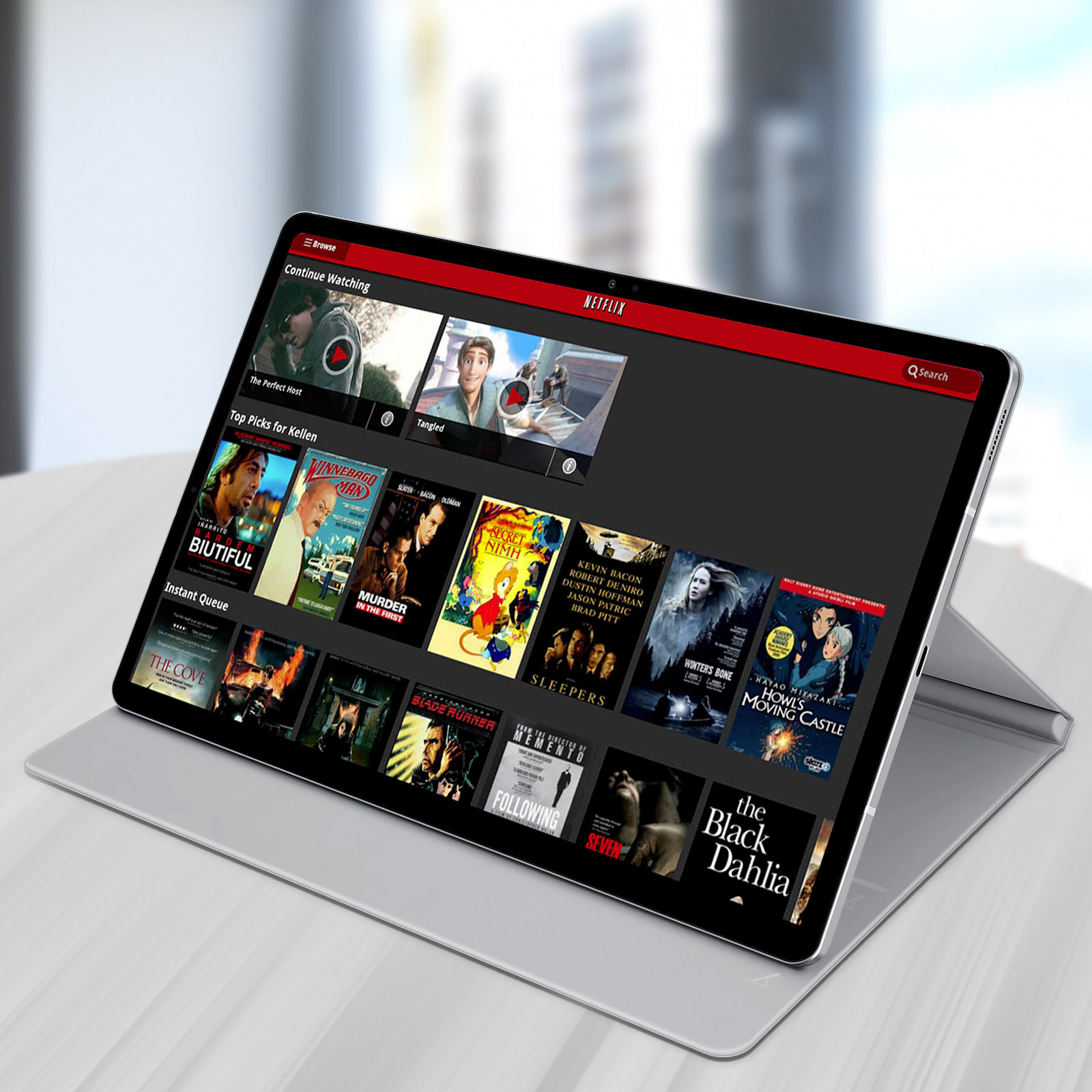 Il tablet mostra l'interfaccia di Netflix. I film sono visualizzati sul tablet, su un supporto, vicino a una finestra.