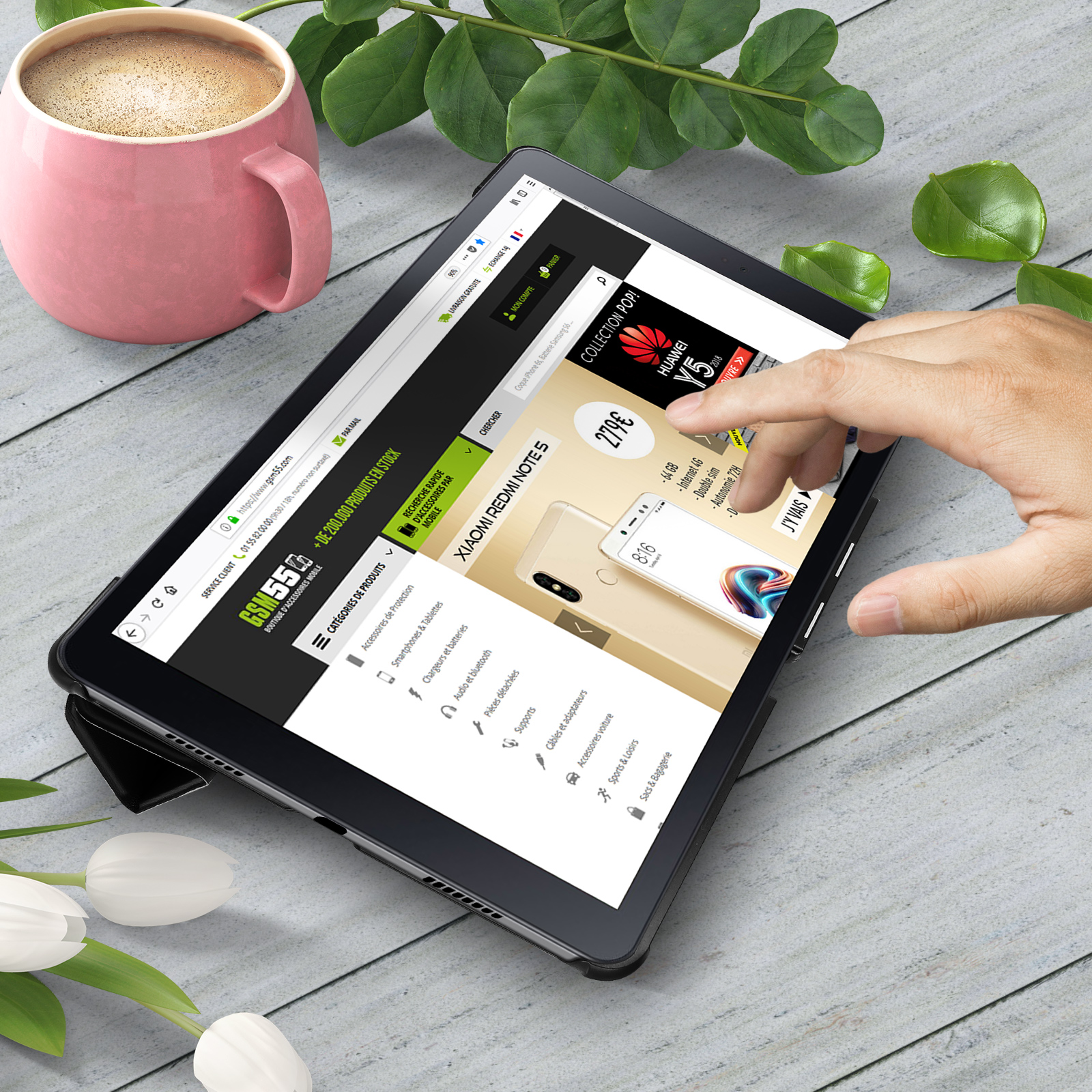 Tablet su una scrivania. Persona che tocca lo schermo. Sito web visibile sullo schermo. Caffè e pianta nelle vicinanze.