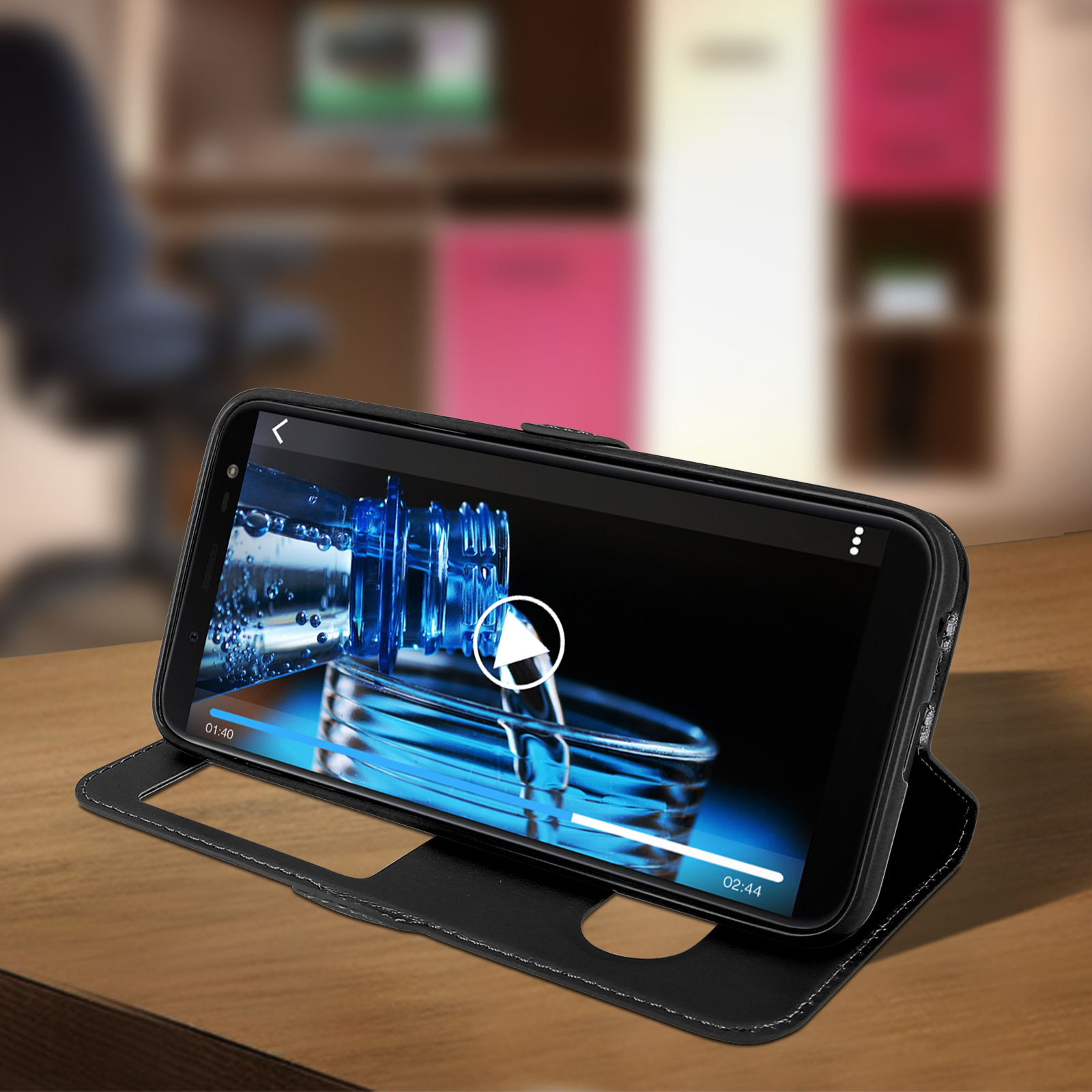 Telefono nero in una custodia, che riproduce un video. La custodia è aperta su un tavolo di legno.