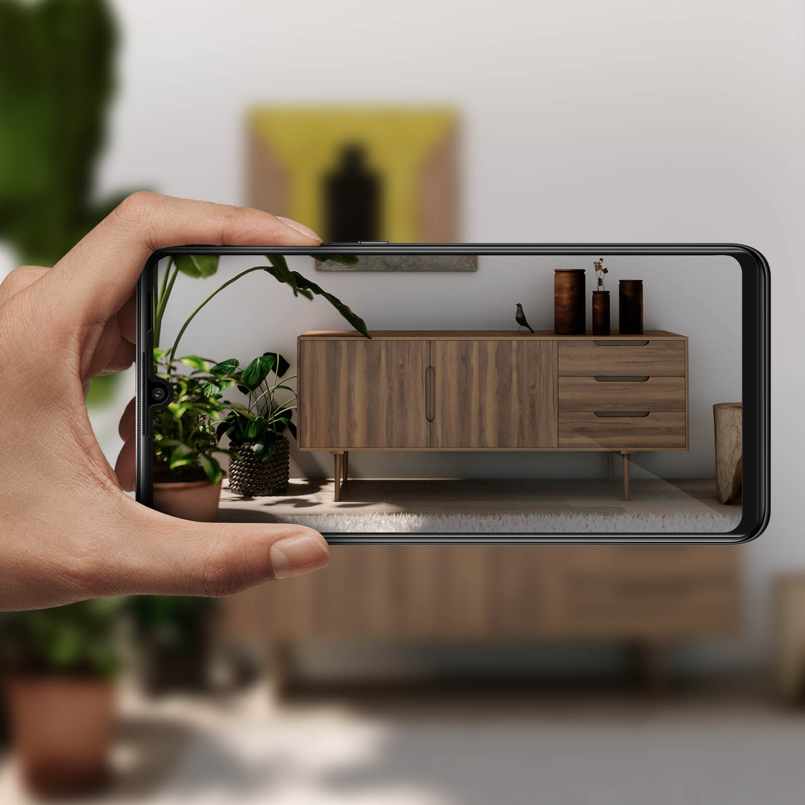 Persona che tiene un telefono che mostra una stanza con mobili. La stanza ha una pianta e mobili in legno.