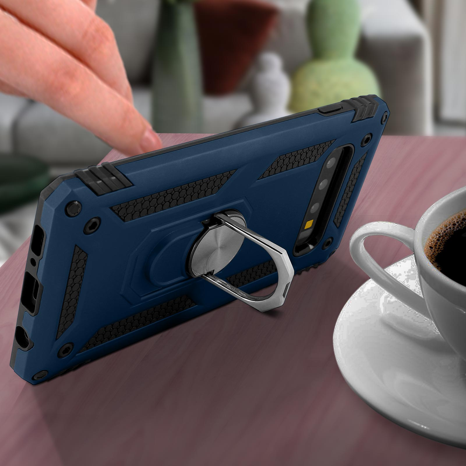 Una custodia blu con anello, su un tavolo. Una mano tocca il telefono.