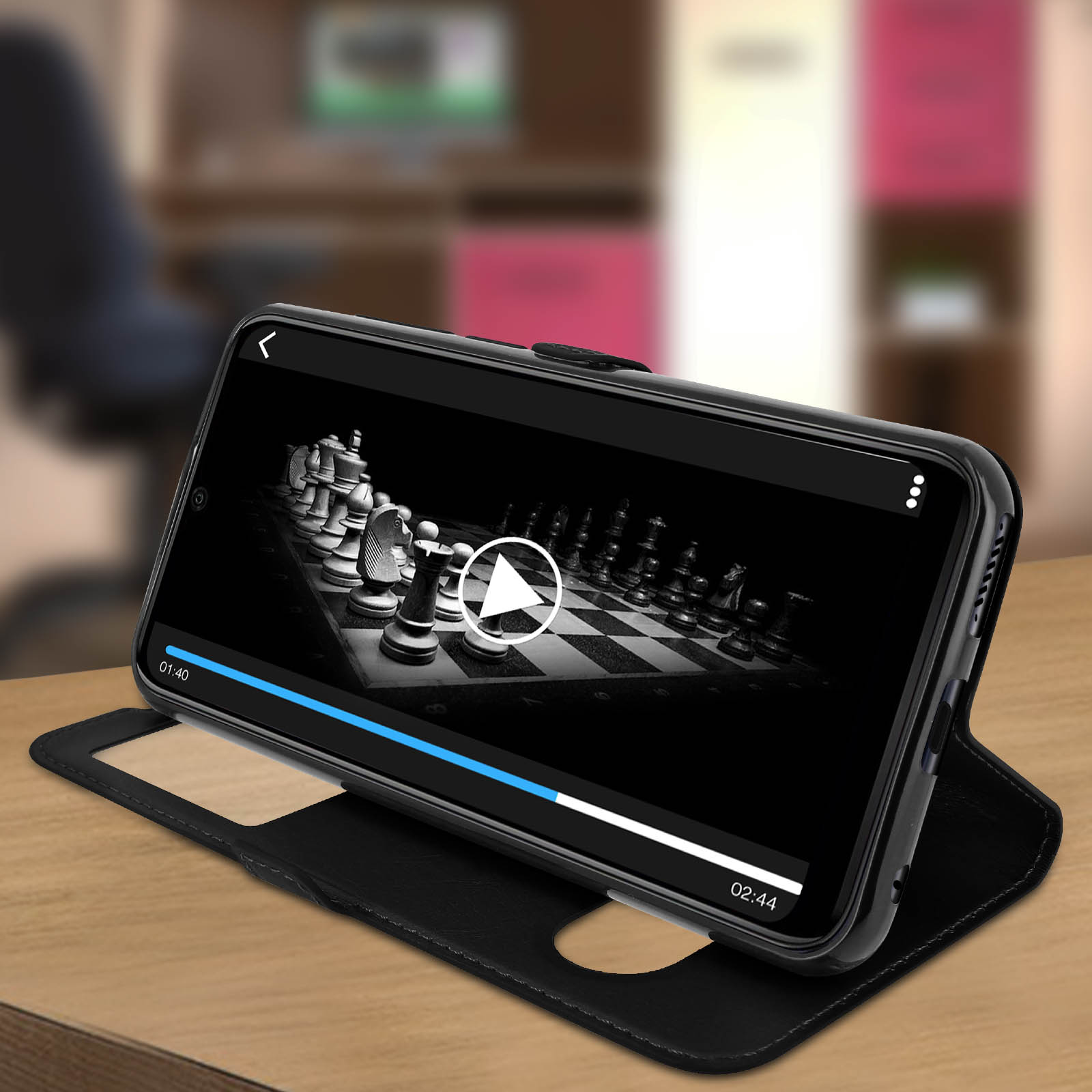 Un téléphone dans un étui noir affichant une vidéo d'échecs. L'étui est ouvert sur une table.