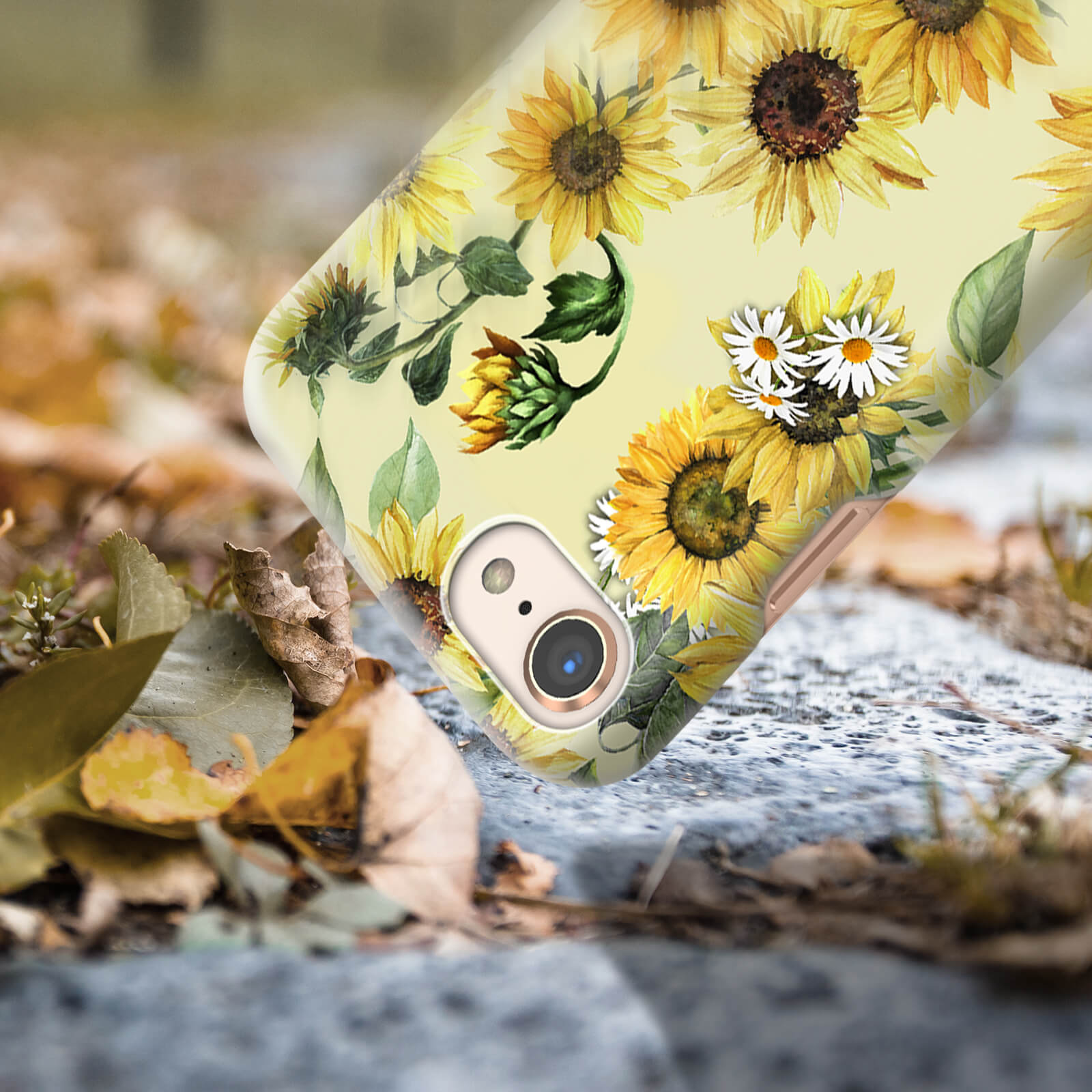 Custodia per telefono con girasoli e margherite. Il telefono è su una superficie di pietra. Lo sfondo ha foglie.