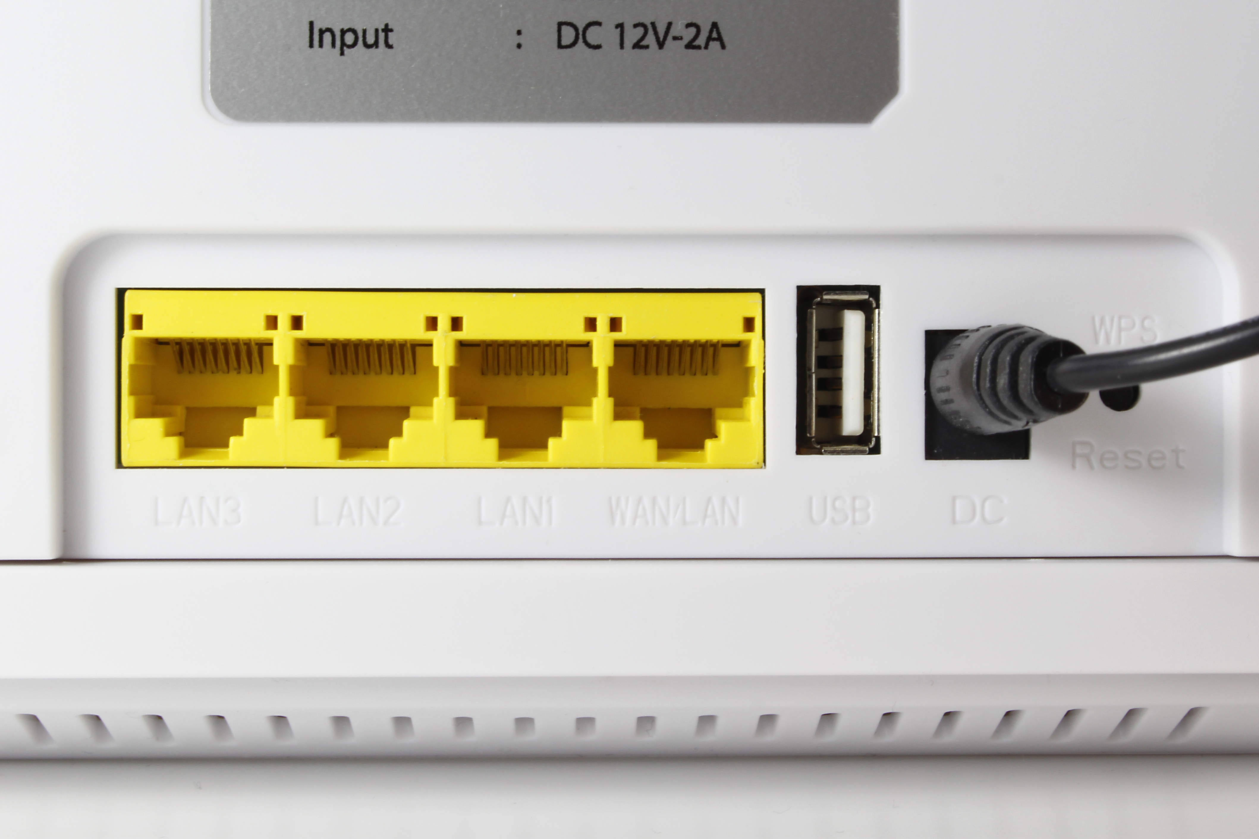 Nahaufnahme der Router-Anschlüsse: gelbe LAN-Anschlüsse, ein USB-Anschluss und ein DC-Eingang. Weißer Hintergrund.