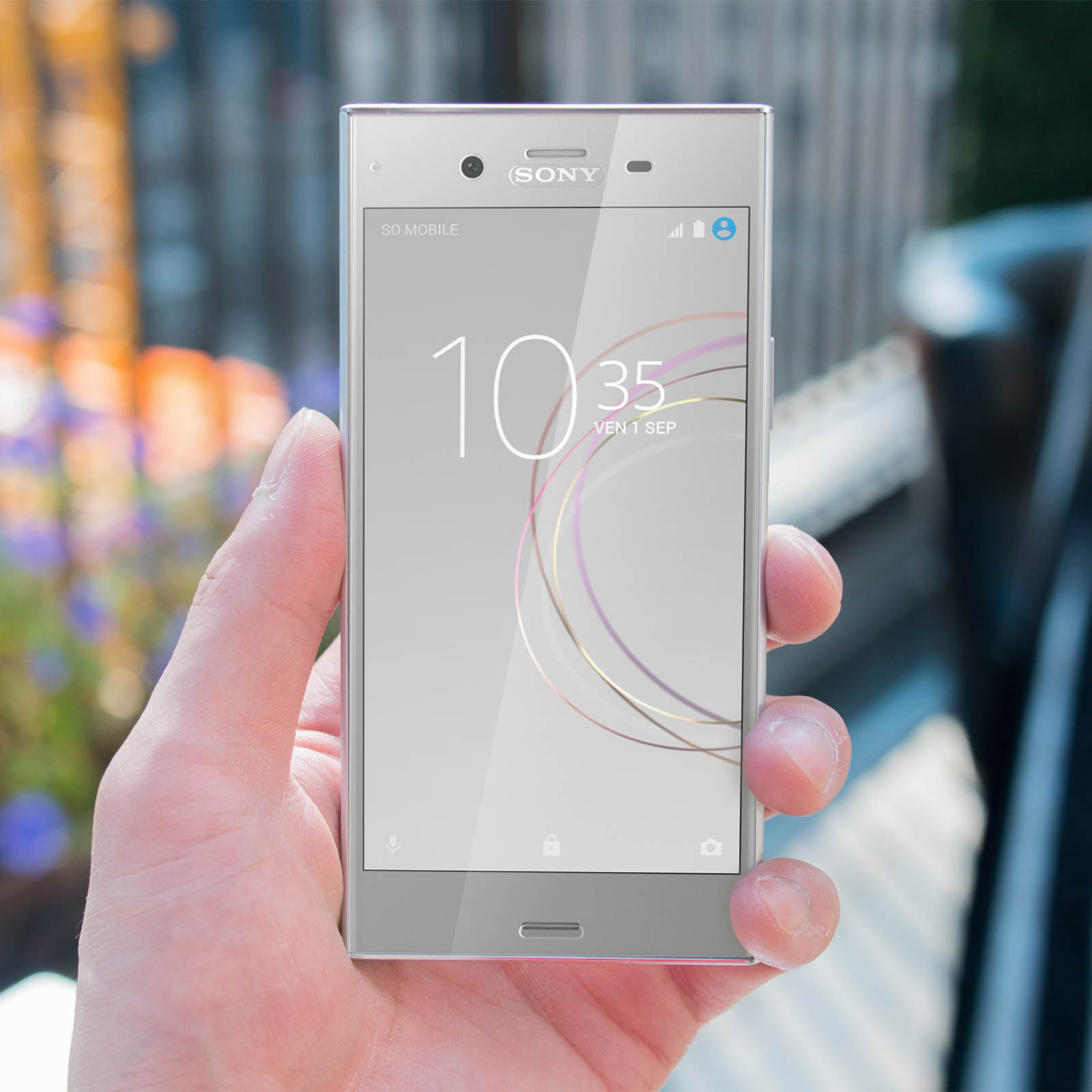 Una mano che tiene un telefono Sony argento che mostra l'ora, sfondo sfocato.