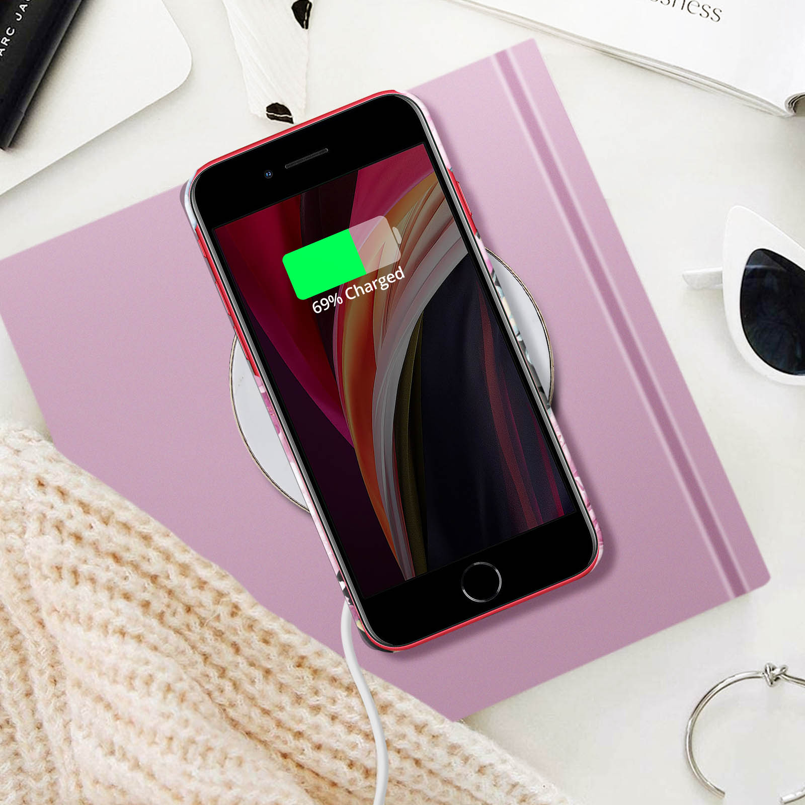 Telefon wird drahtlos auf rosa Pad geladen, verschiedene Gegenstände auf dem Tisch.