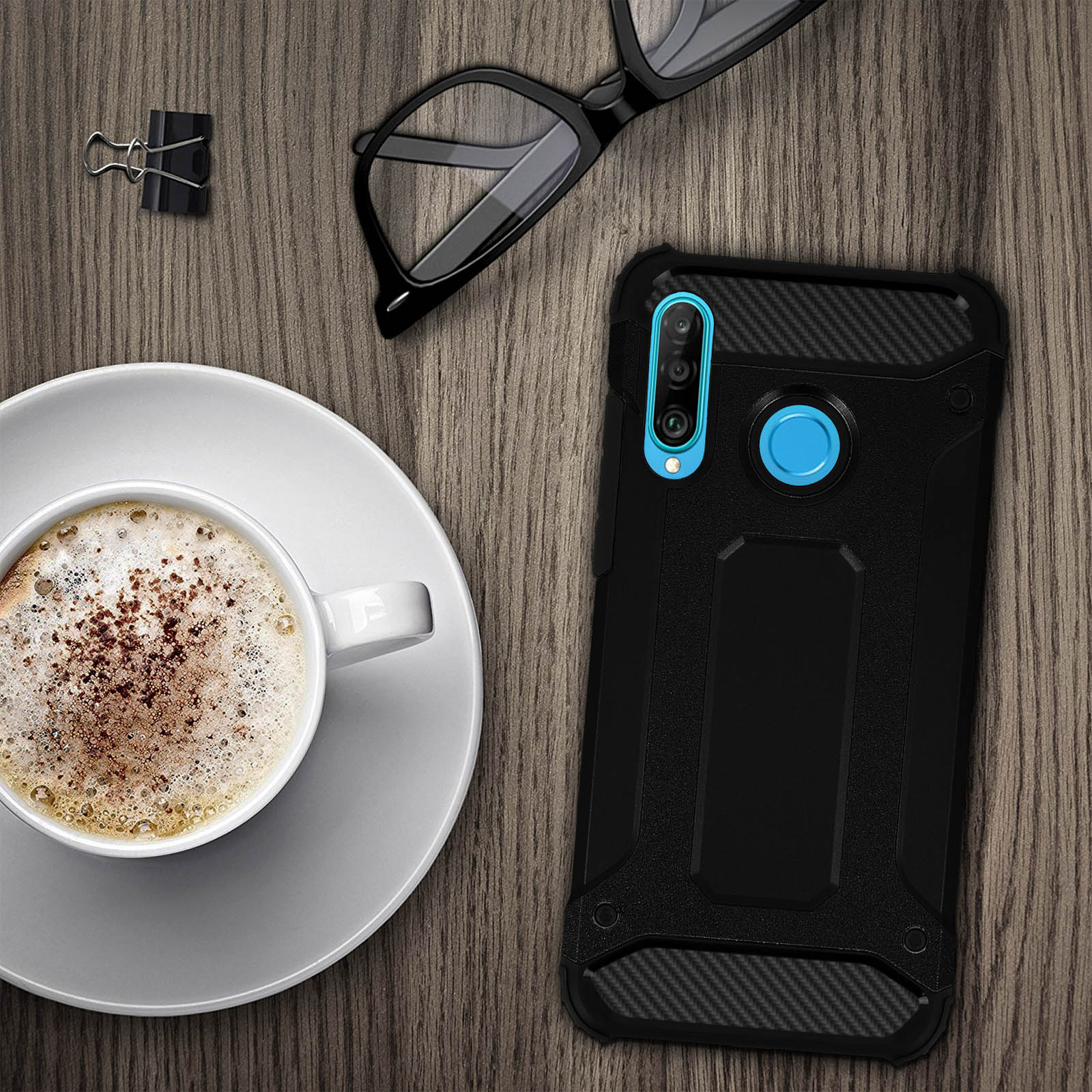 Custodia nera per telefono, caffè con schiuma, occhiali e graffetta su un tavolo di legno.