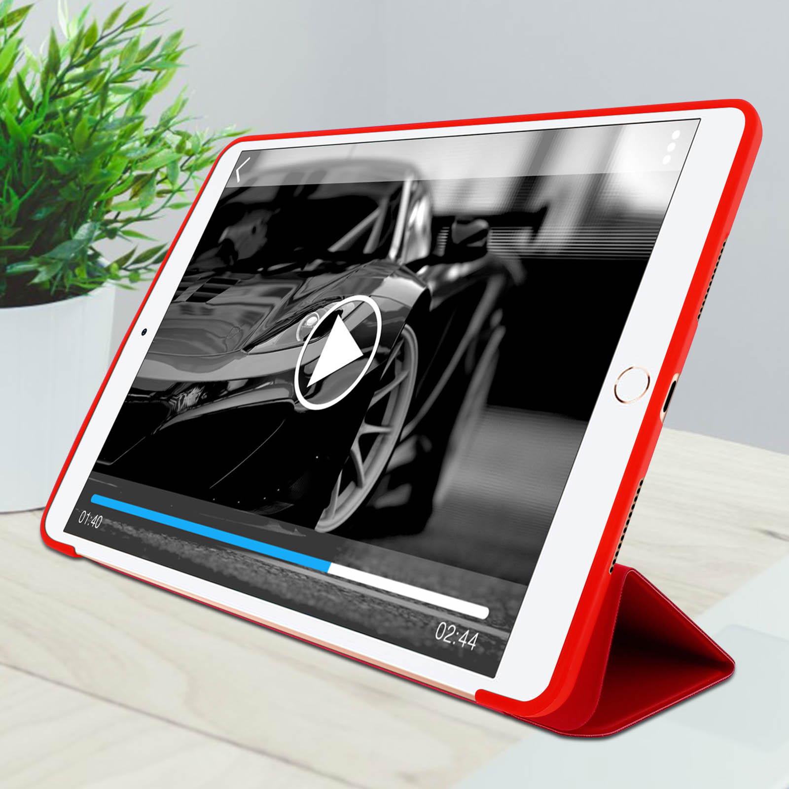 Tablet che mostra un video di un'auto, in una custodia rossa. Una pianta è a sinistra.