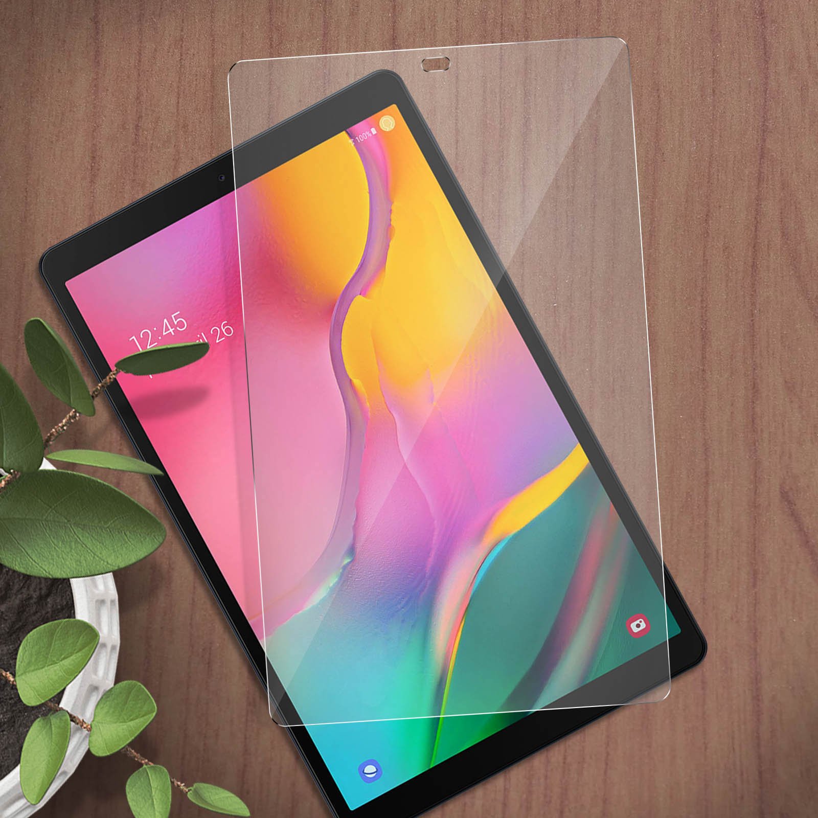 Une tablette avec un protecteur d'écran appliqué, posée sur une table en bois à côté d'une plante.