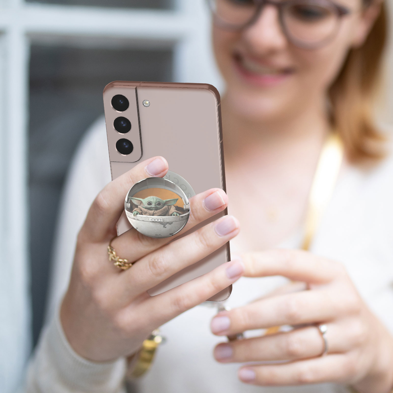 Eine Frau hält ein Telefon. Das Telefon hat einen Pop-Socket mit Baby Yoda drauf. Das Telefon ist pink.