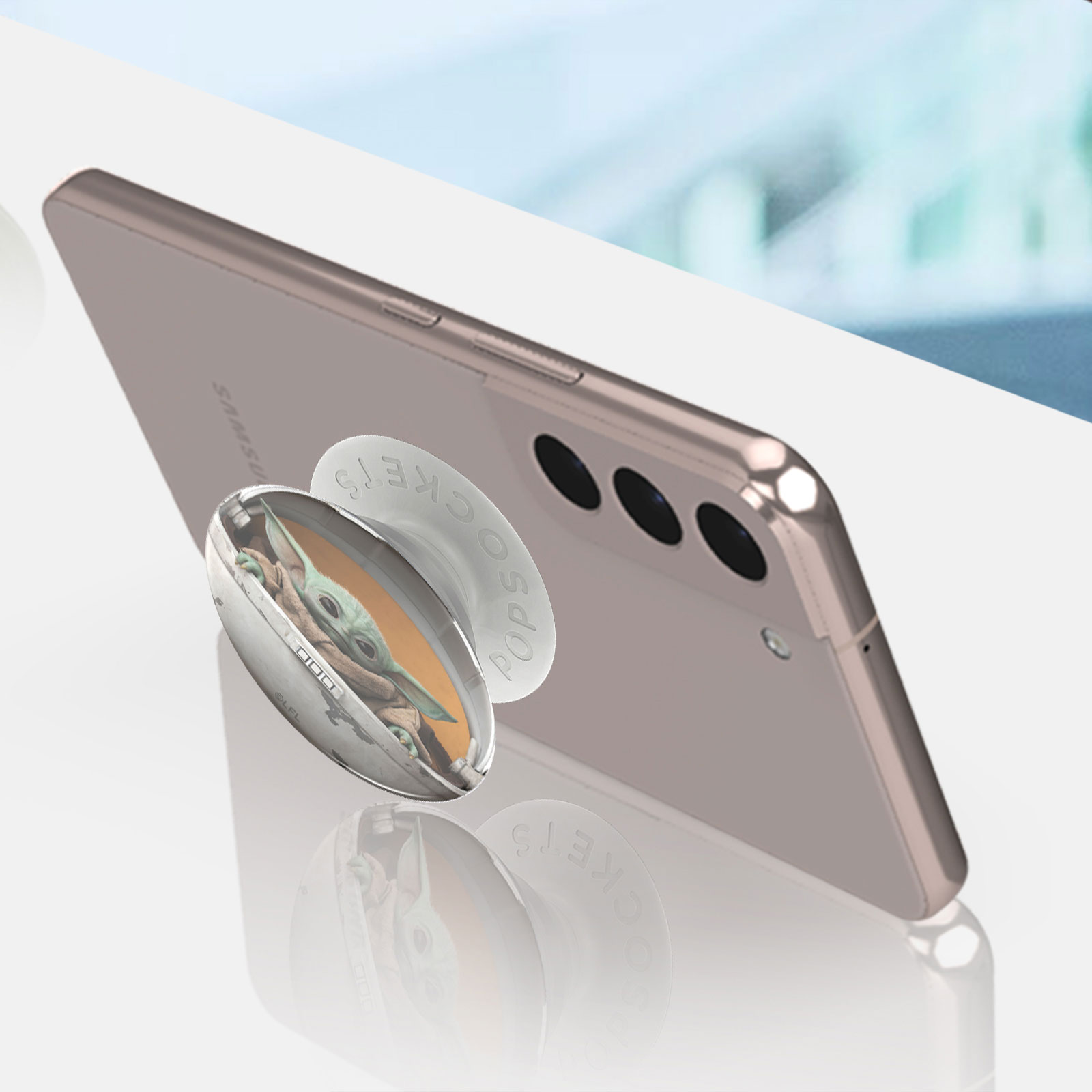 Ein Smartphone mit einem Baby Yoda PopSocket, das sich auf einer weißen Oberfläche spiegelt.