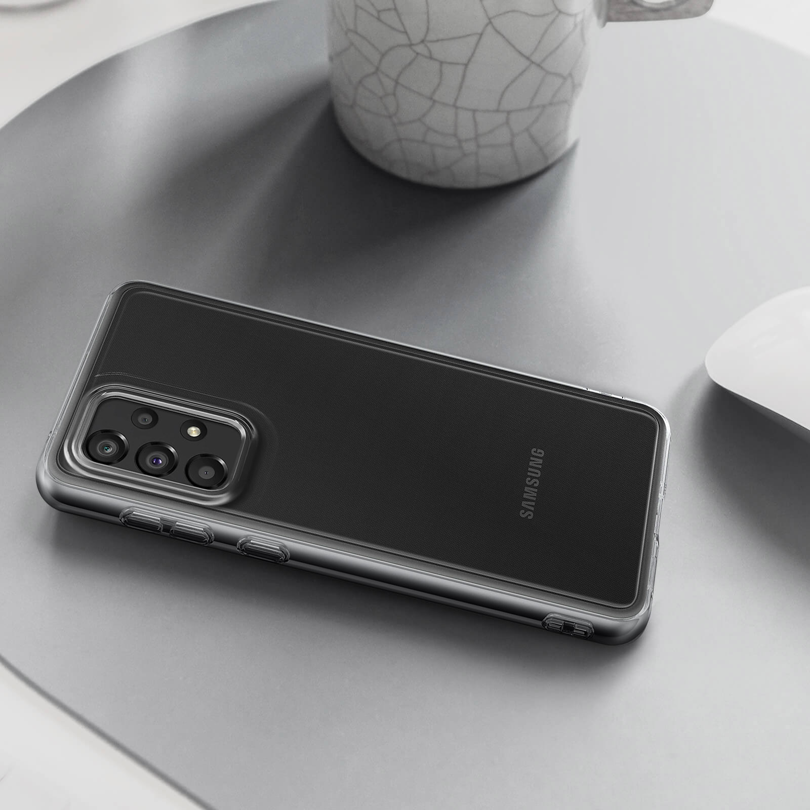 Transparente Handyhülle auf silberner Oberfläche. Telefon ist schwarz, mit mehreren Kameras. Maus im Hintergrund.