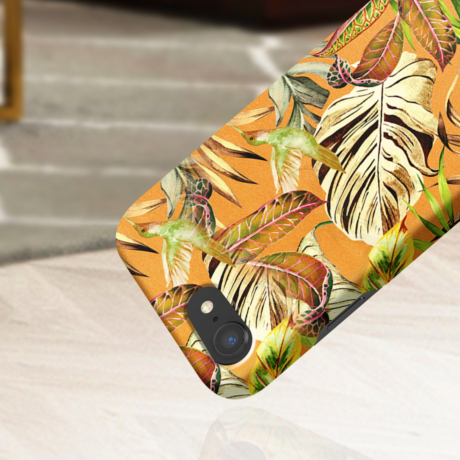 Custodia per telefono con design floreale e foglie. Sfondo arancione, luce che cade.