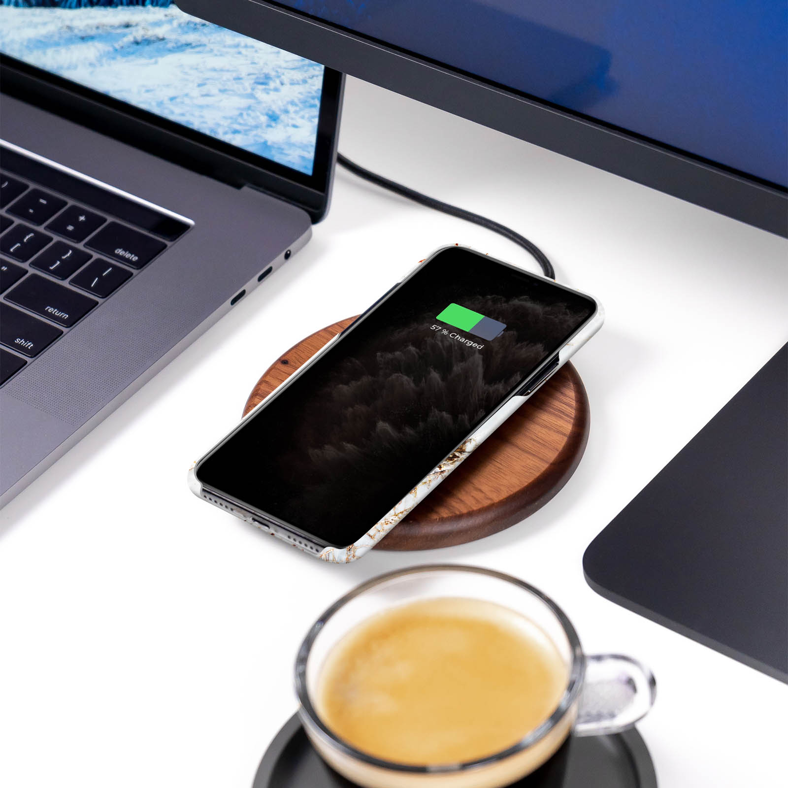 Telefon wird auf kabellosem Holzladegerät geladen. Laptop und Kaffeetasse daneben.