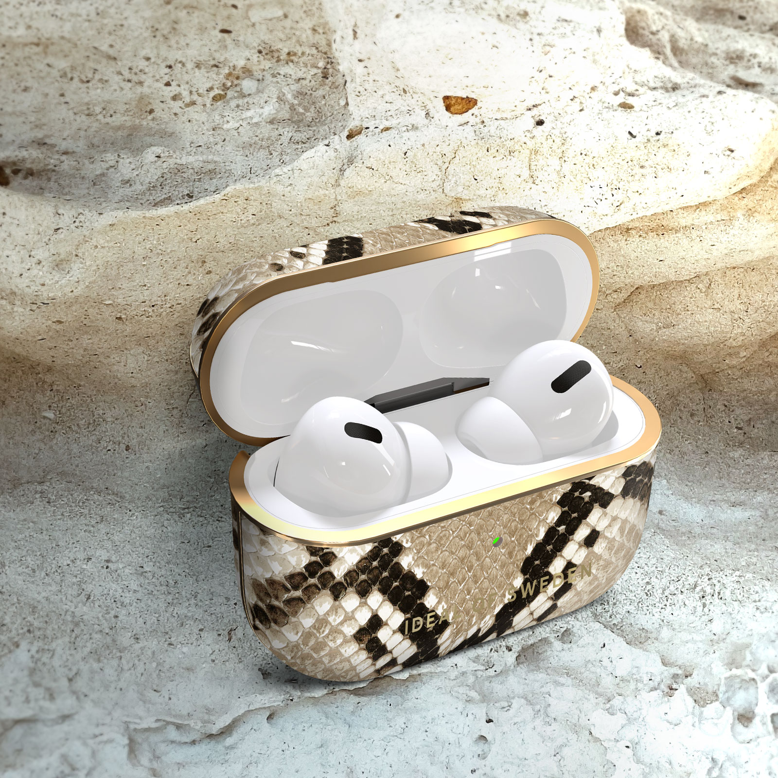 Auriculares en un estuche con estampado de piel de serpiente, abierto sobre piedra. Ribete dorado.