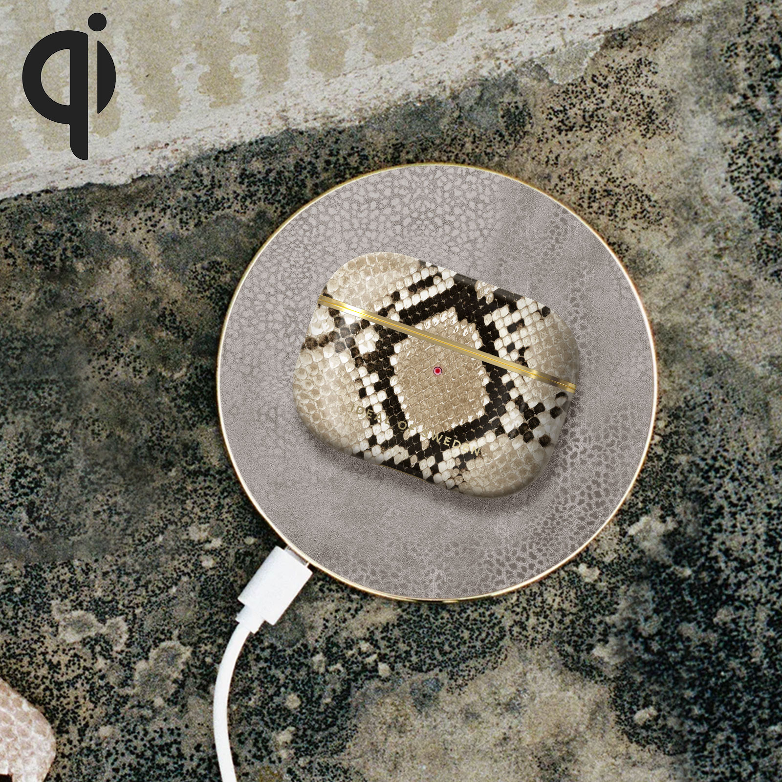 Funda de AirPods en un cargador inalámbrico. El cargador es gris con un anillo dorado. Cable blanco conectado.