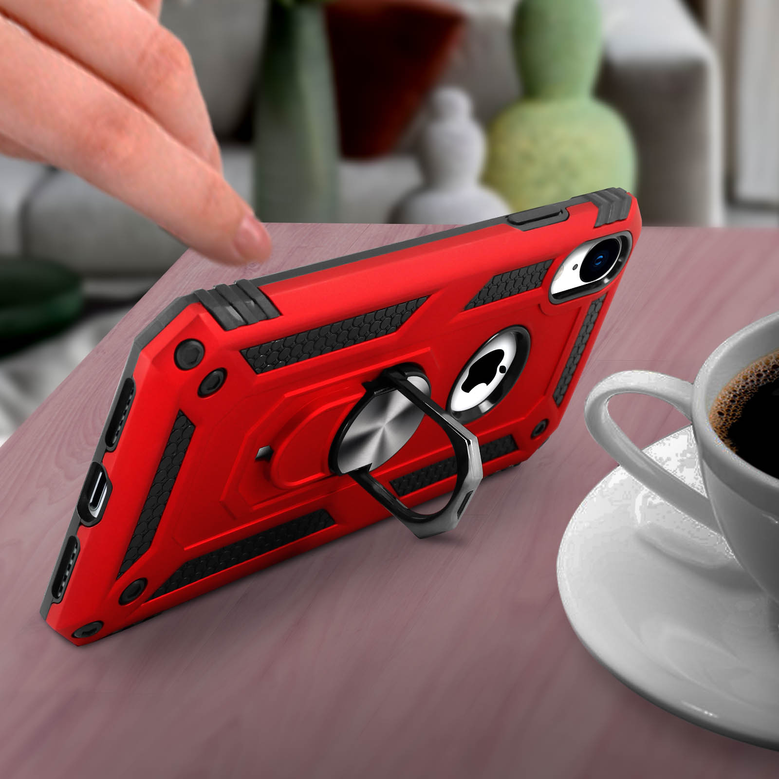 Una custodia rossa per telefono con supporto ad anello su una superficie di legno. È presente una tazza di caffè.