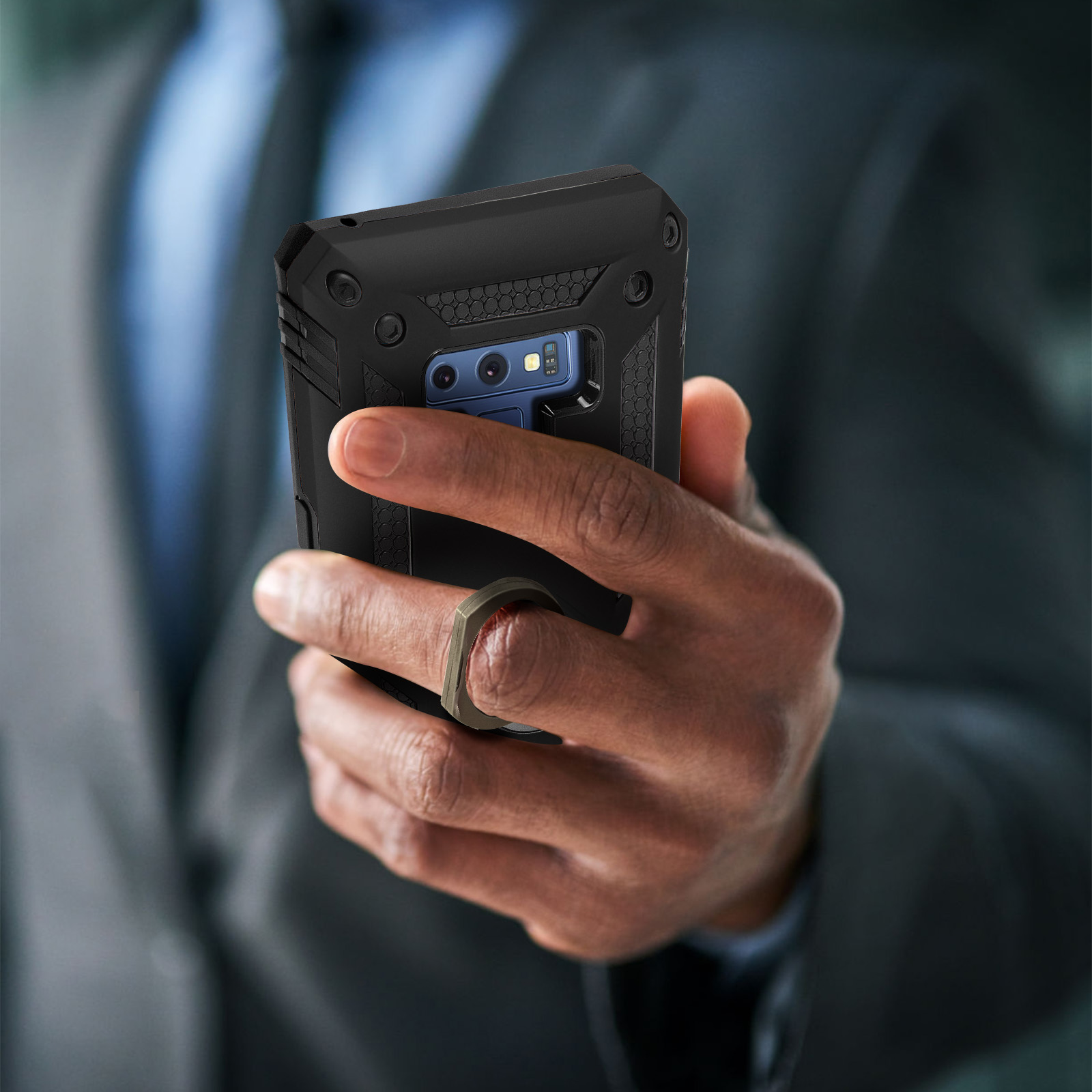 La mano di una persona che tiene un telefono nero con un porta anello sul retro, che indossa un abito.