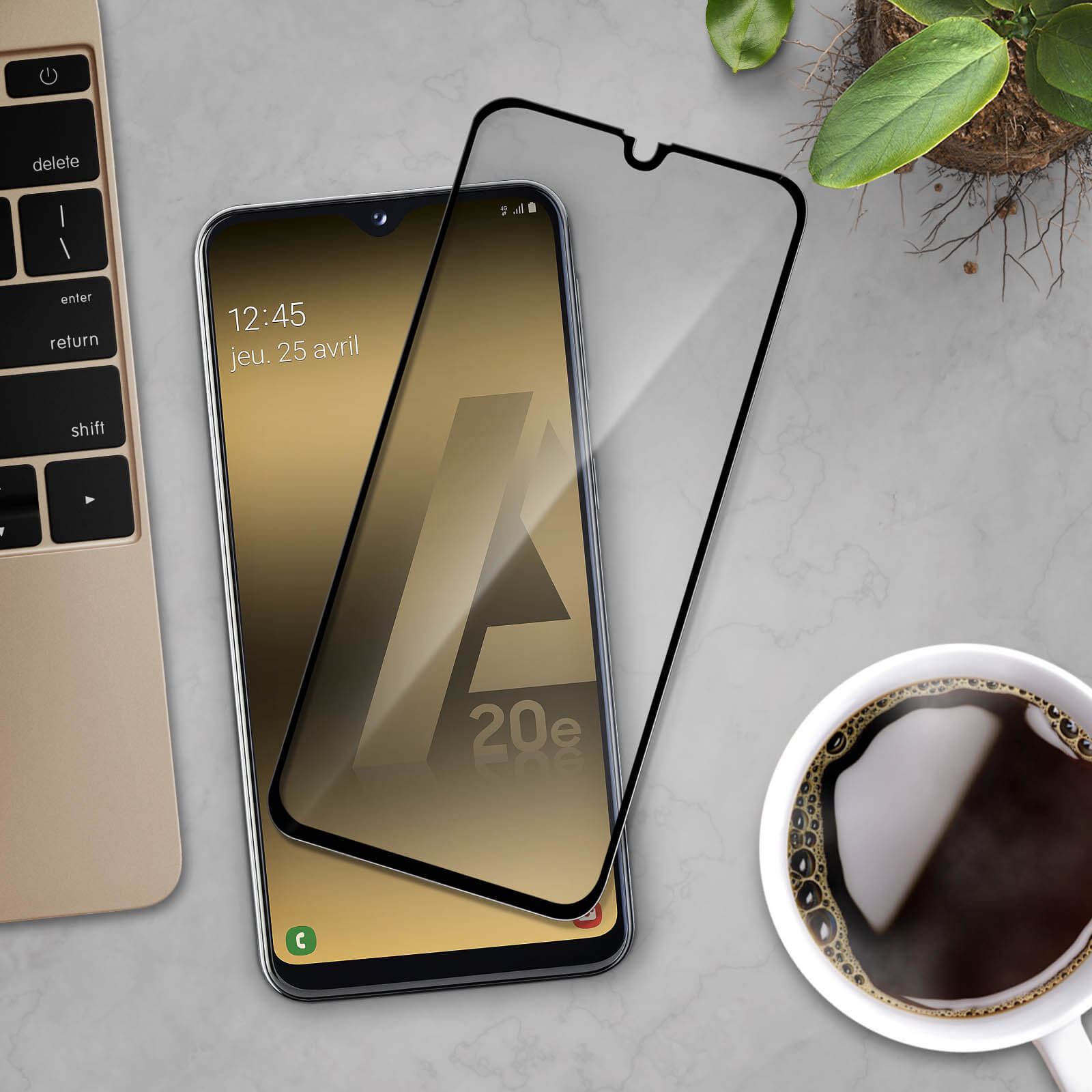 Smartphone con protezione schermo, tazza di caffè e pianta. Il telefono visualizza la data. Lo sfondo è chiaro.