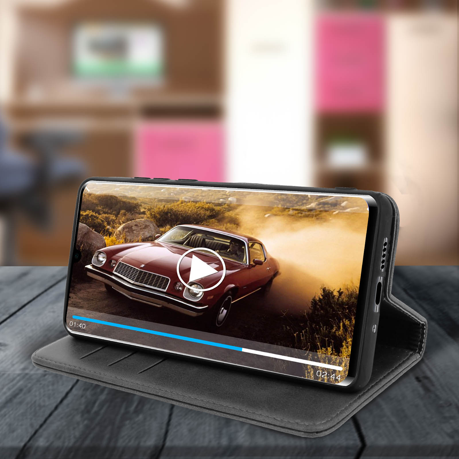 Custodia per smartphone con video di auto d'epoca in riproduzione, su tavolo di legno.