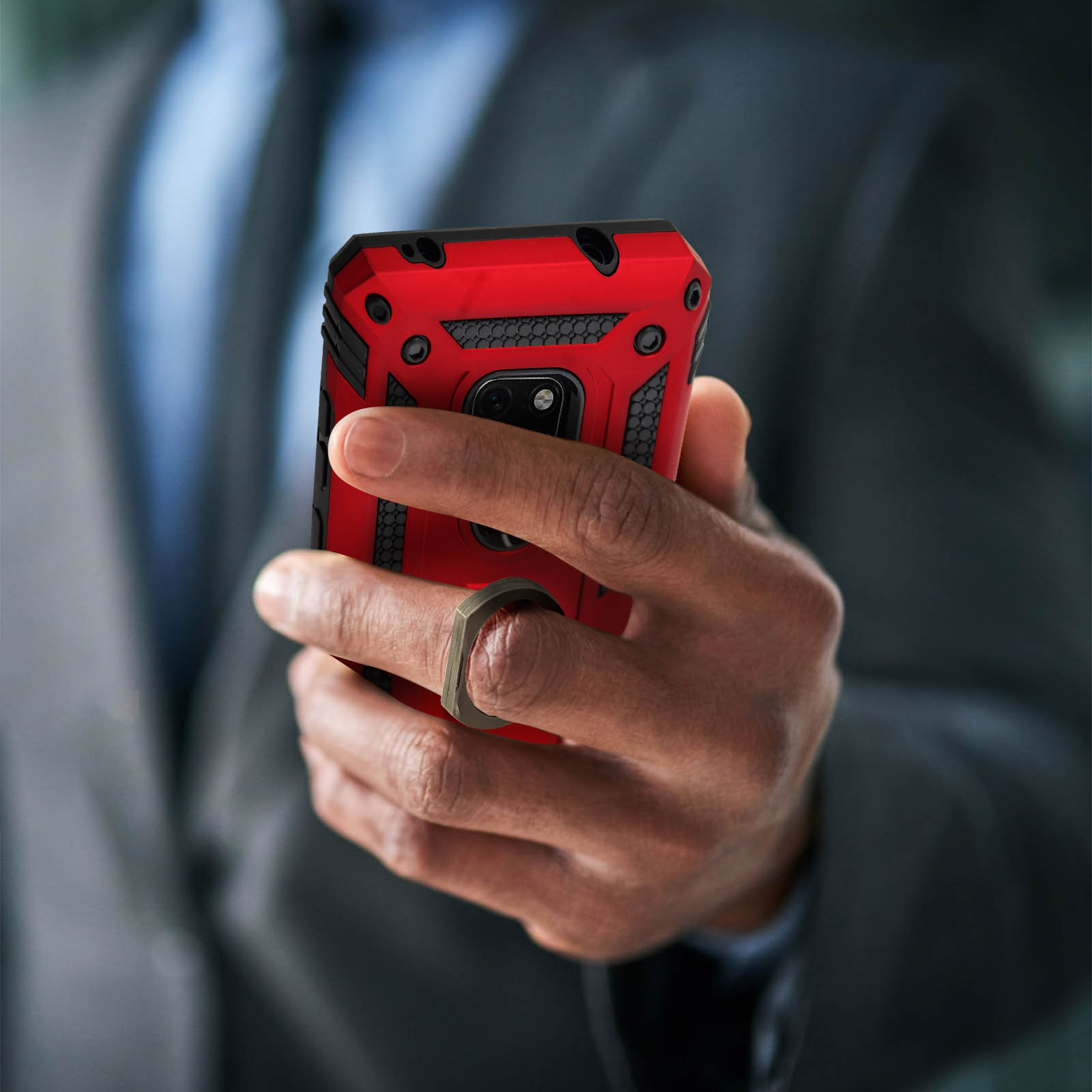 Main tenant un téléphone avec un étui rouge. L'étui a un anneau. Le fond est un costume.