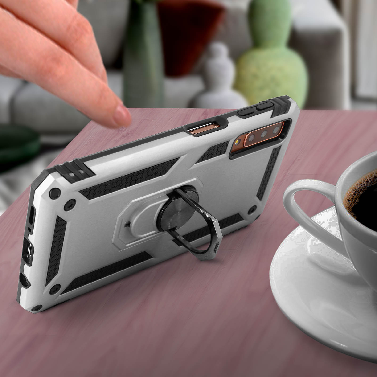 Silberne Handyhülle mit Ringhalter, auf einem Tisch mit Kaffeetasse daneben.