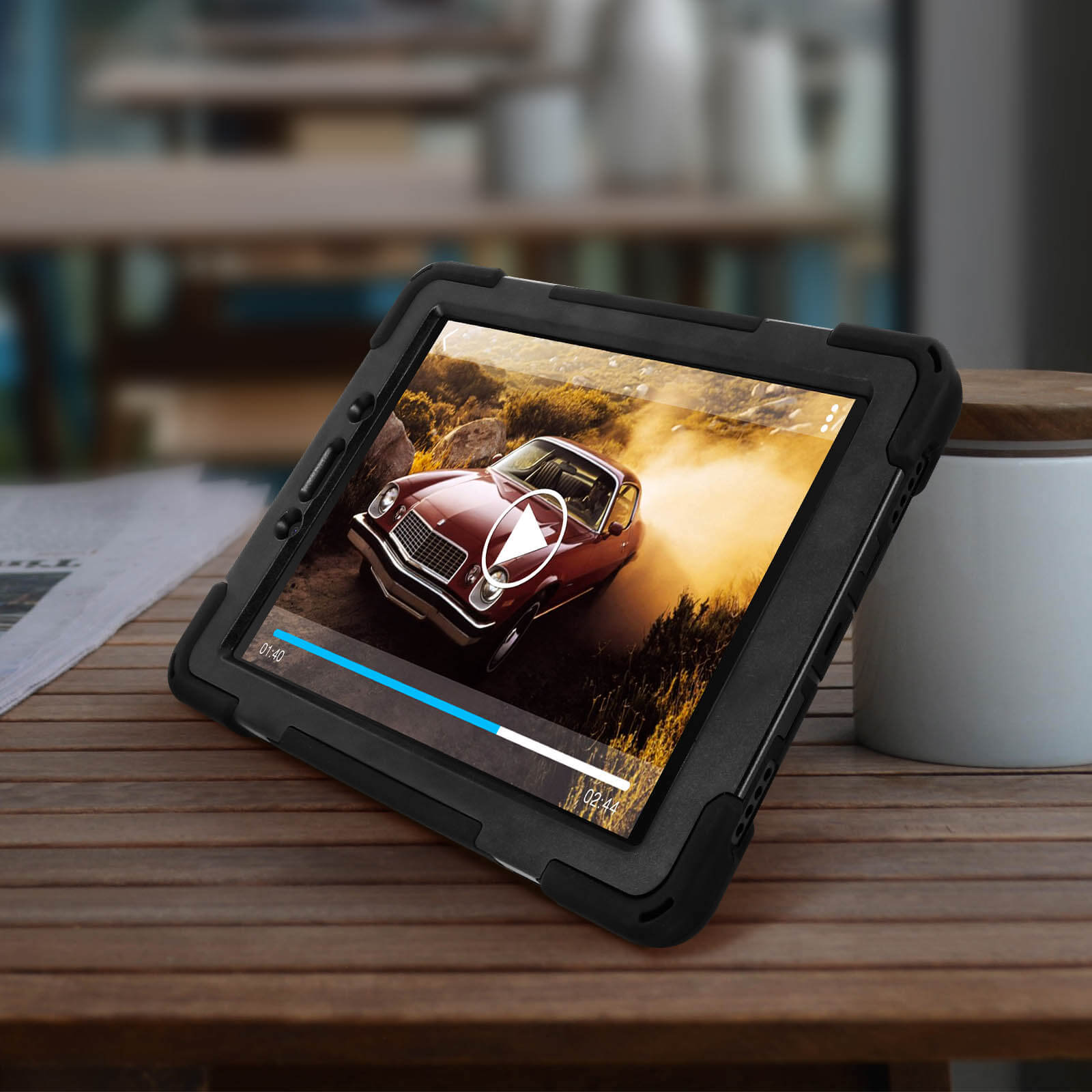 Ein Tablet in einer schwarzen Hülle, das ein Video eines klassischen roten Autos auf einem Holztisch abspielt.