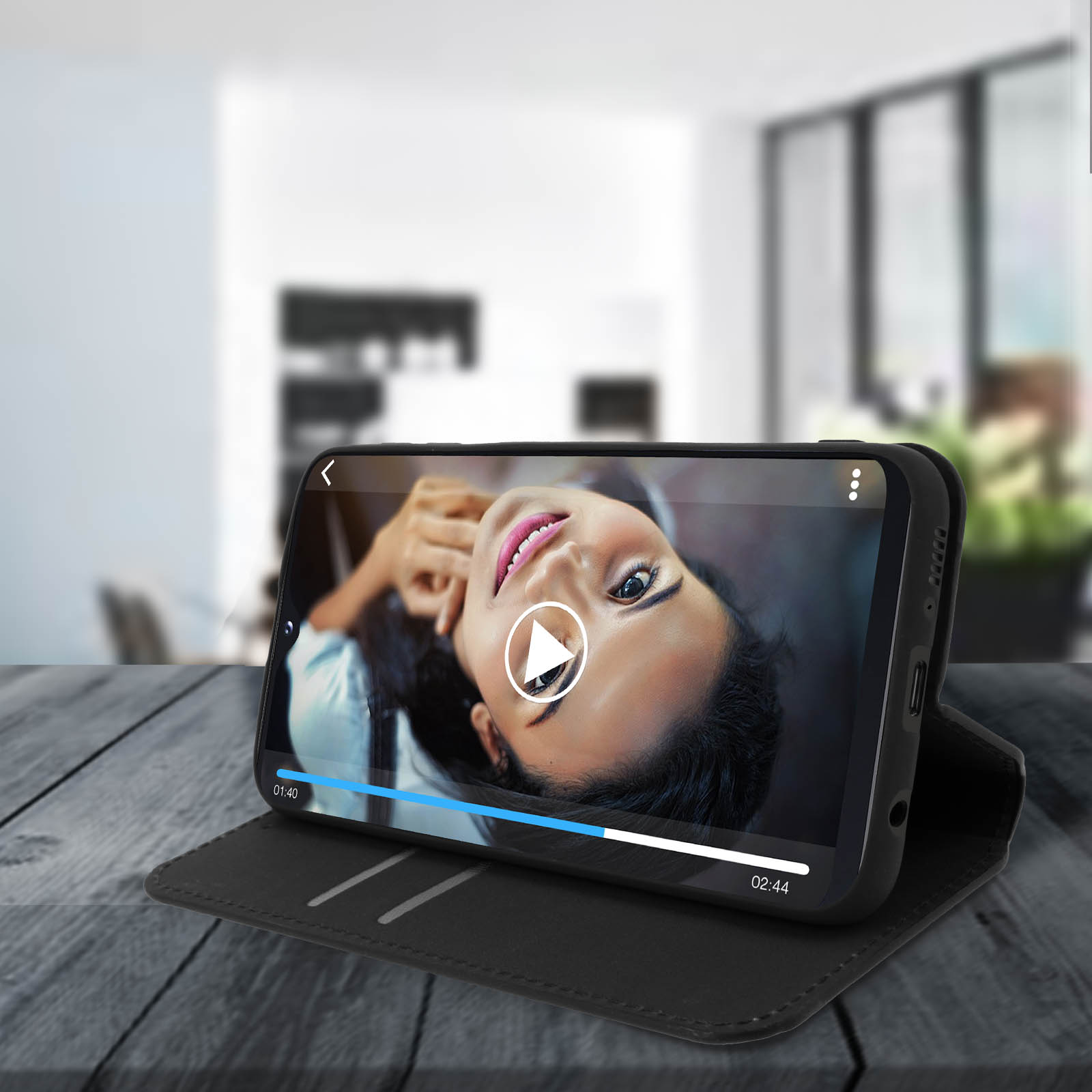 Un téléphone affiche une vidéo d'une femme. Le téléphone est dans un étui noir et posé sur une surface en bois.