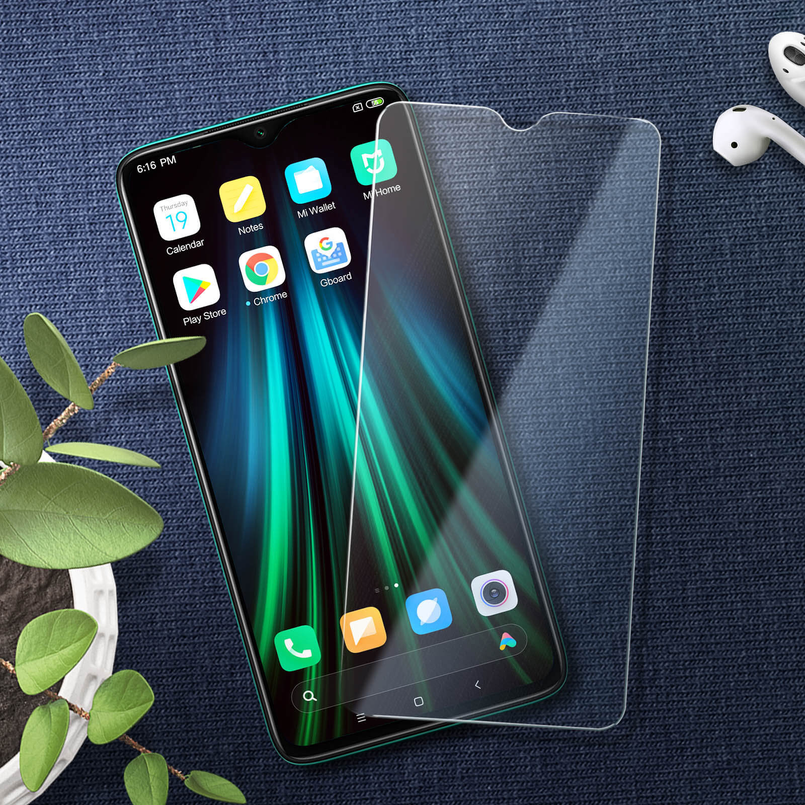 Telefono verde con protezione schermo. App visibili. Auricolari sullo sfondo, su superficie blu.
