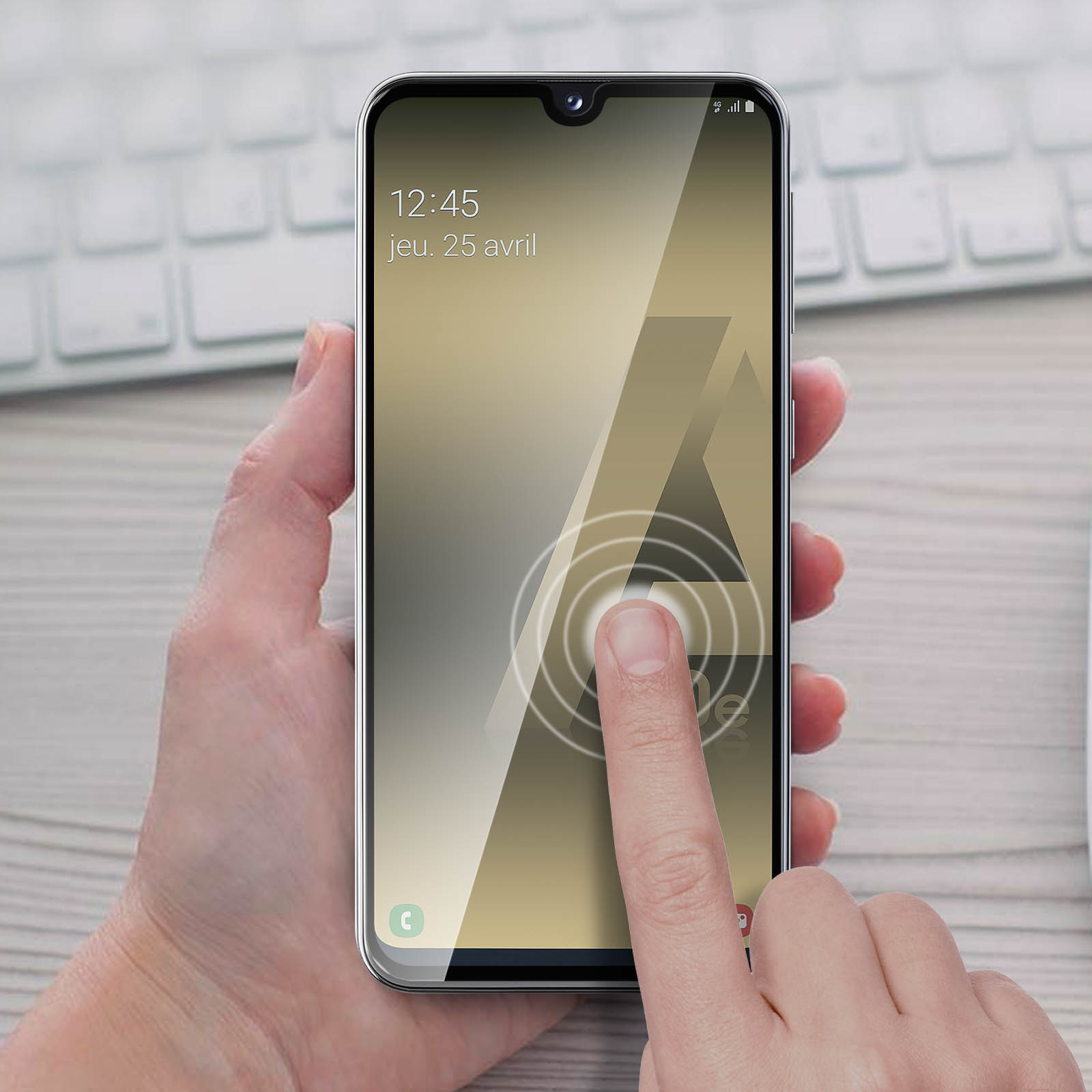 Une main touchant l'écran d'un téléphone. Le téléphone affiche la date et la lettre A. Le fond est un bureau.