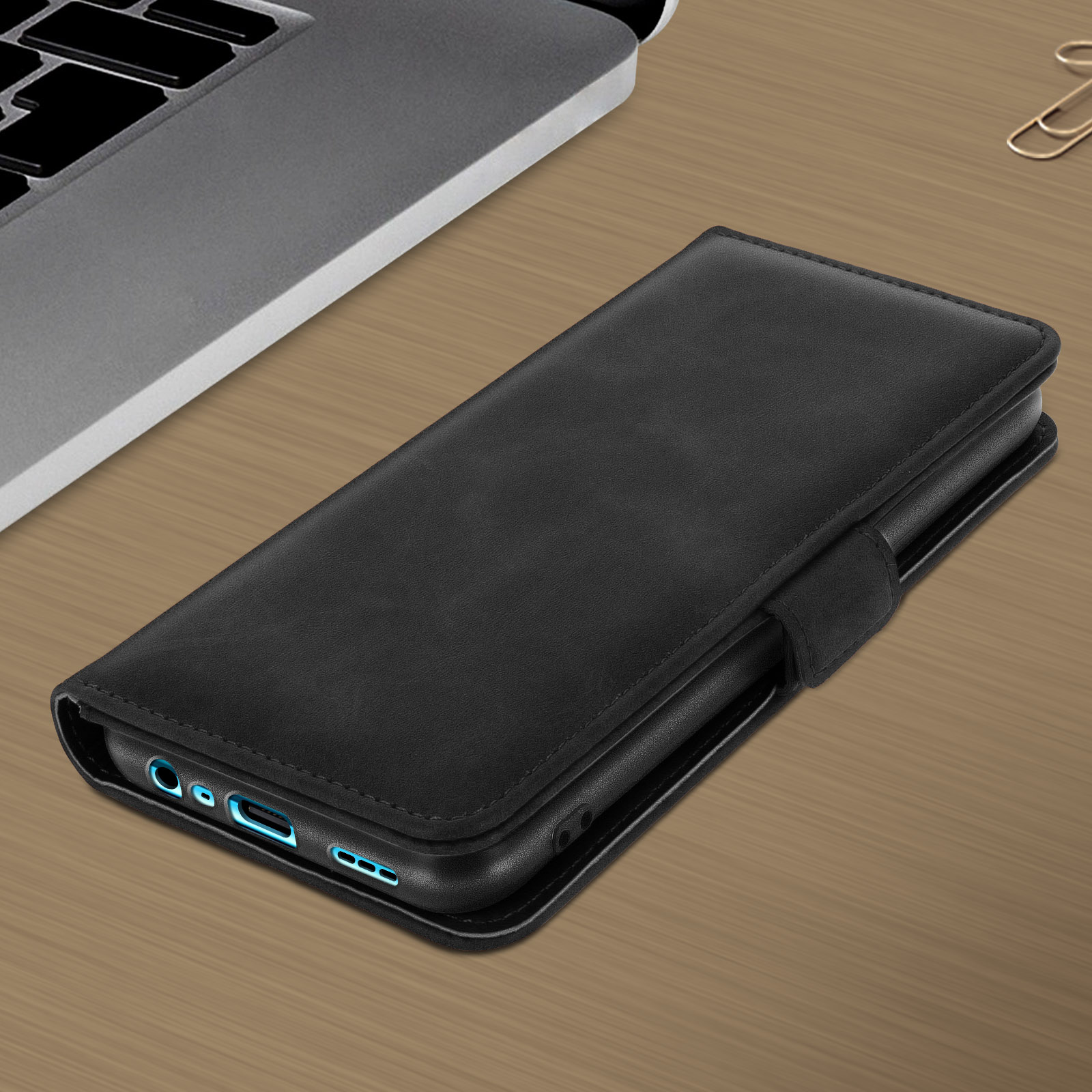 Custodia per telefono nera, chiusa, su una superficie di legno, con un laptop e un portapenne sullo sfondo.