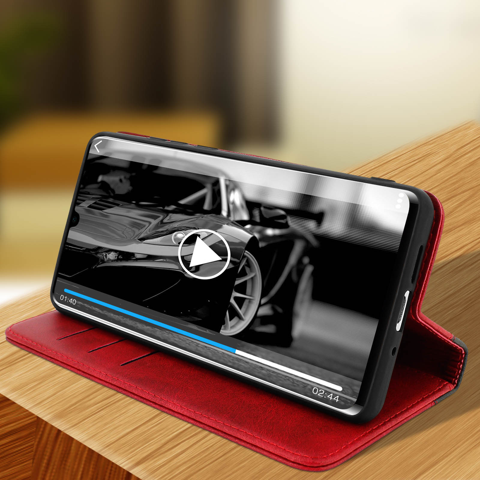 Telefono in custodia rossa mostra un video. Auto nera sullo sfondo.