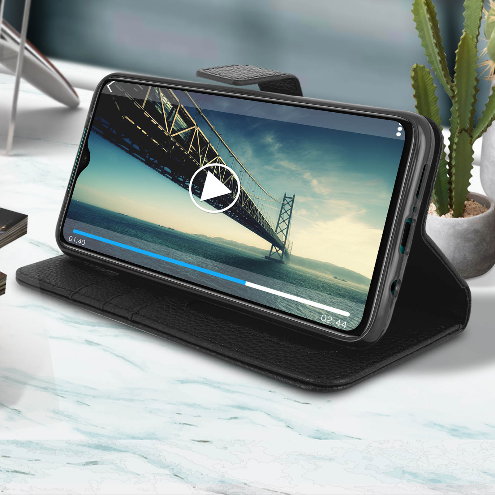 Téléphone noir dans un étui, affichant une vidéo en cours de lecture, avec un pont en arrière-plan.