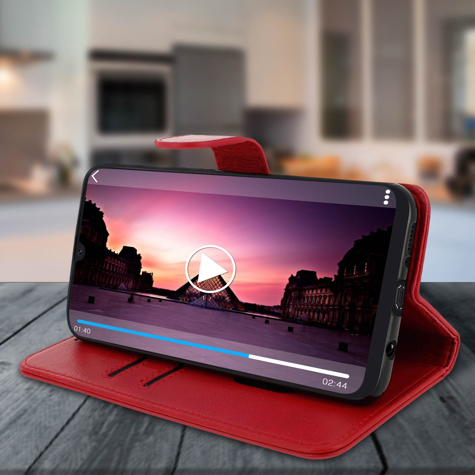 Custodia rossa con telefono che mostra video di una città al tramonto. Custodia aperta su tavolo di legno. Sfondo sfocato della cucina.