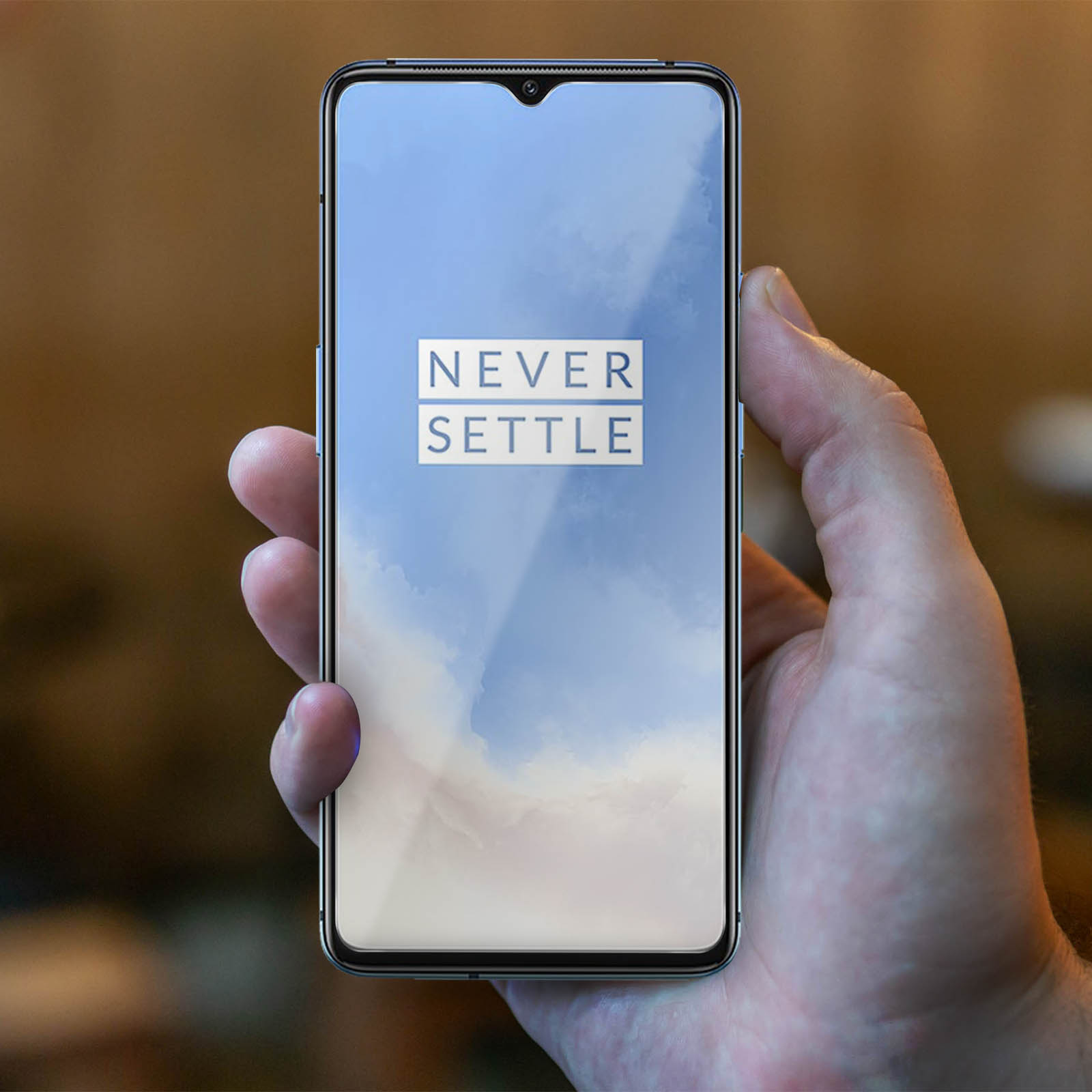 Mano che tiene un telefono con lo schermo che dice 'NEVER SETTLE'. Sfondo sfocato.