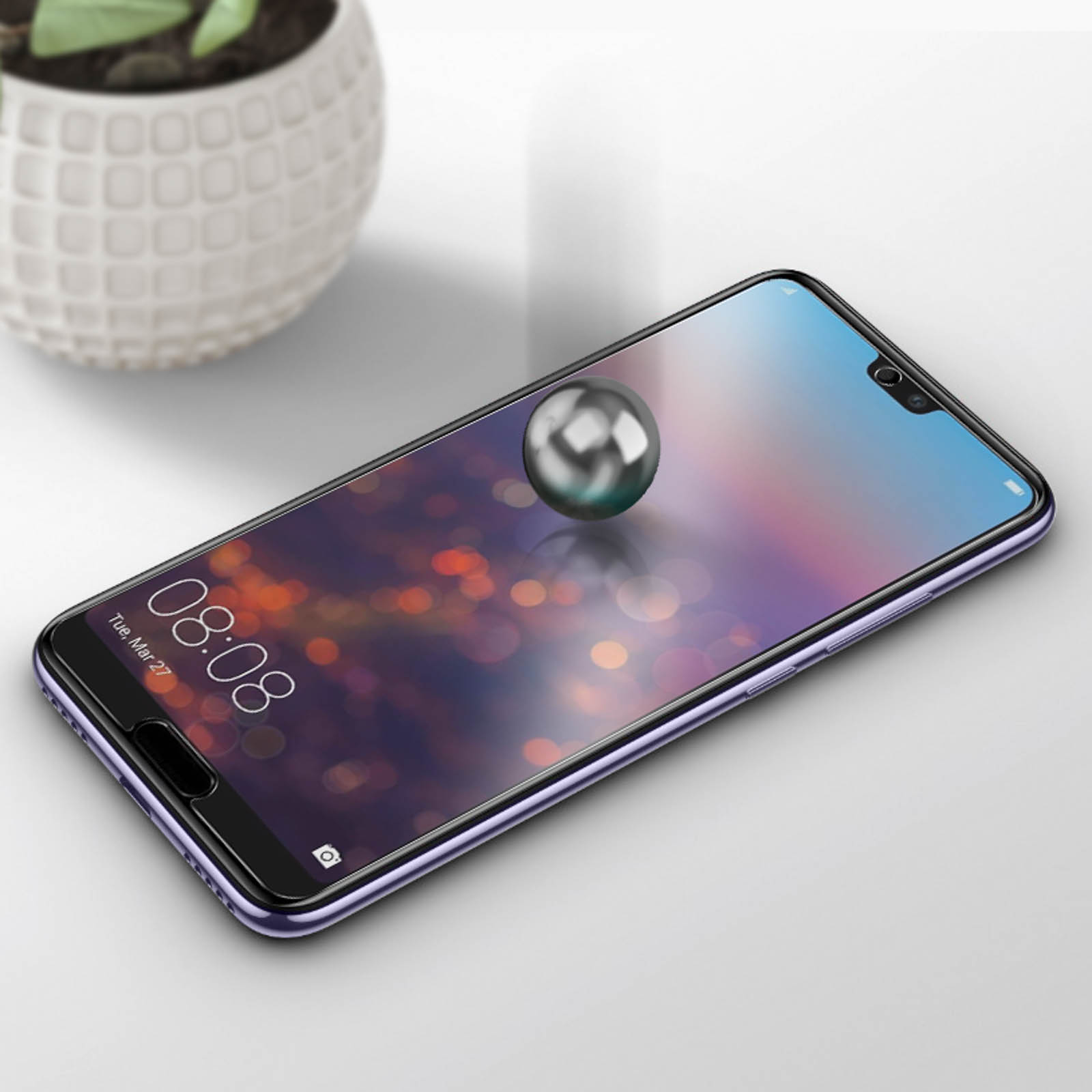 Smartphone con protezione schermo. Una sfera cromata fluttua sopra lo schermo. Lo sfondo è un tavolo bianco.