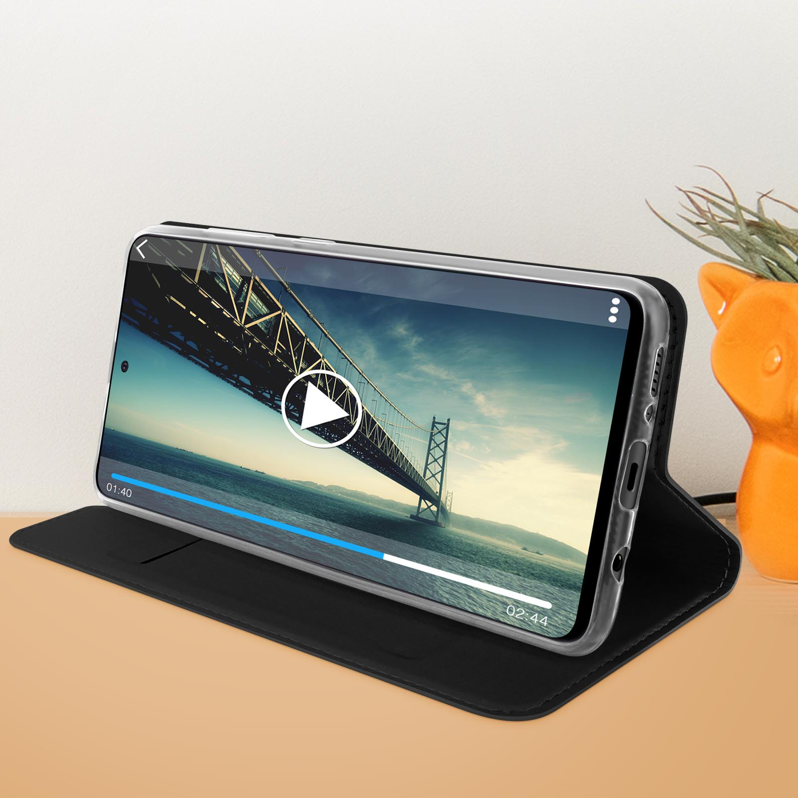Een telefoon in een foliohoes die een video afspeelt met een brug op de achtergrond.