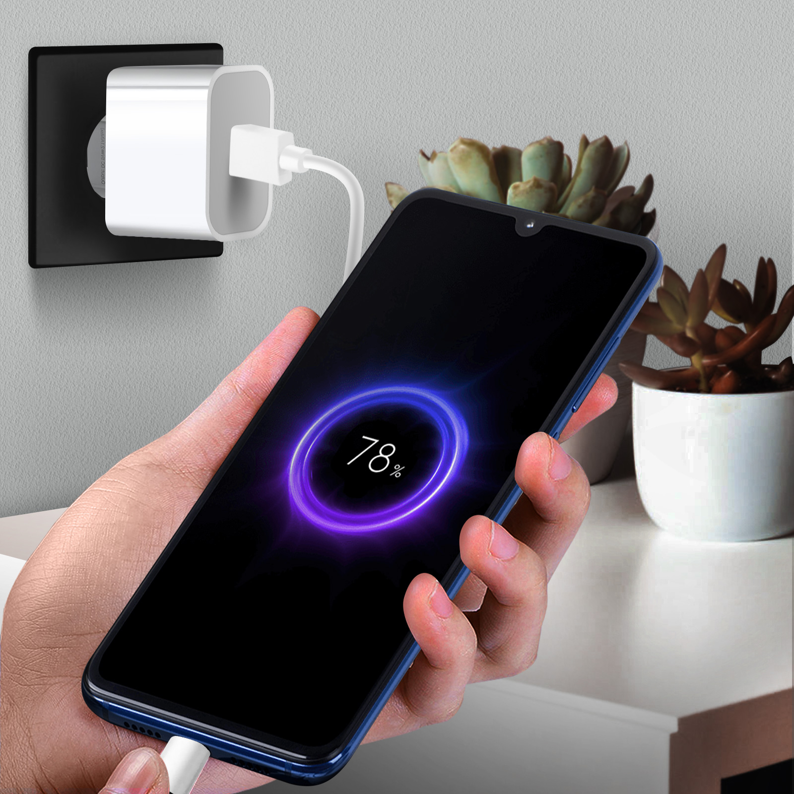 Un telefono in carica con un cavo collegato a una presa a muro e una piccola pianta.