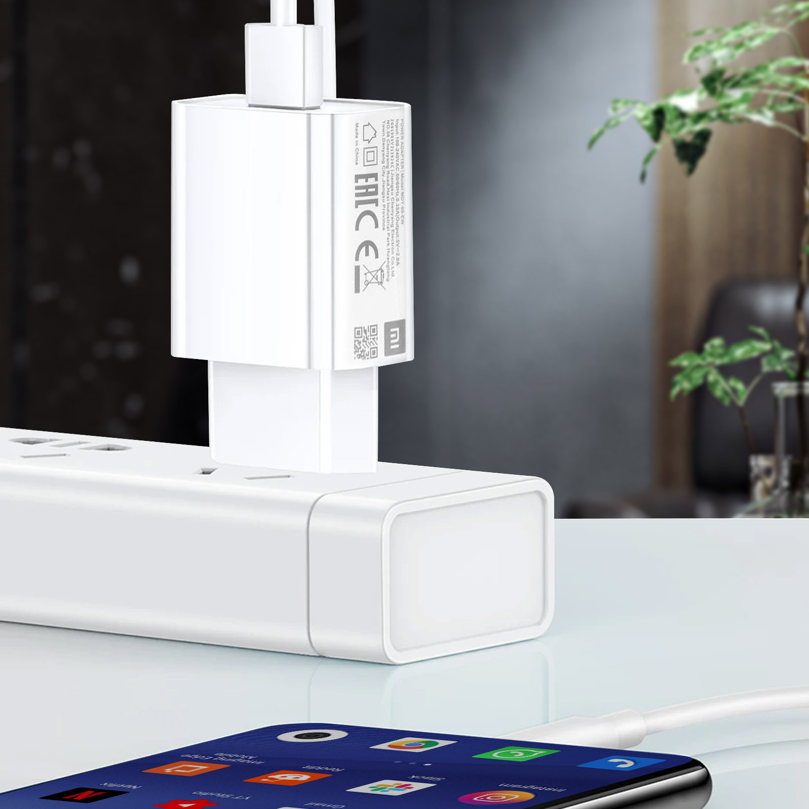 Caricabatterie bianco collegato a una presa, con un telefono in carica in primo piano.