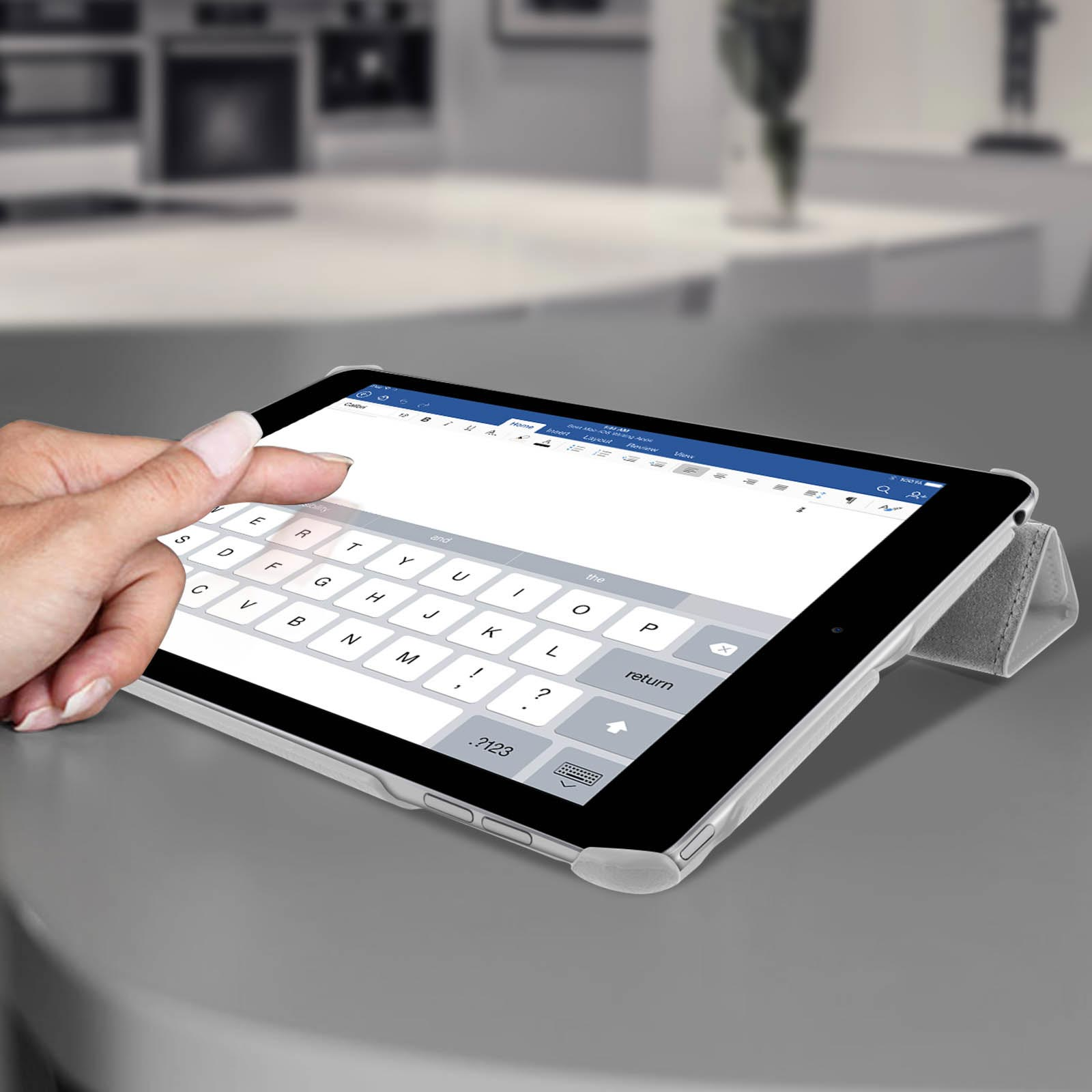 Tablet con interfaccia tastiera, una mano tocca lo schermo. Lo sfondo mostra una cucina sfocata.