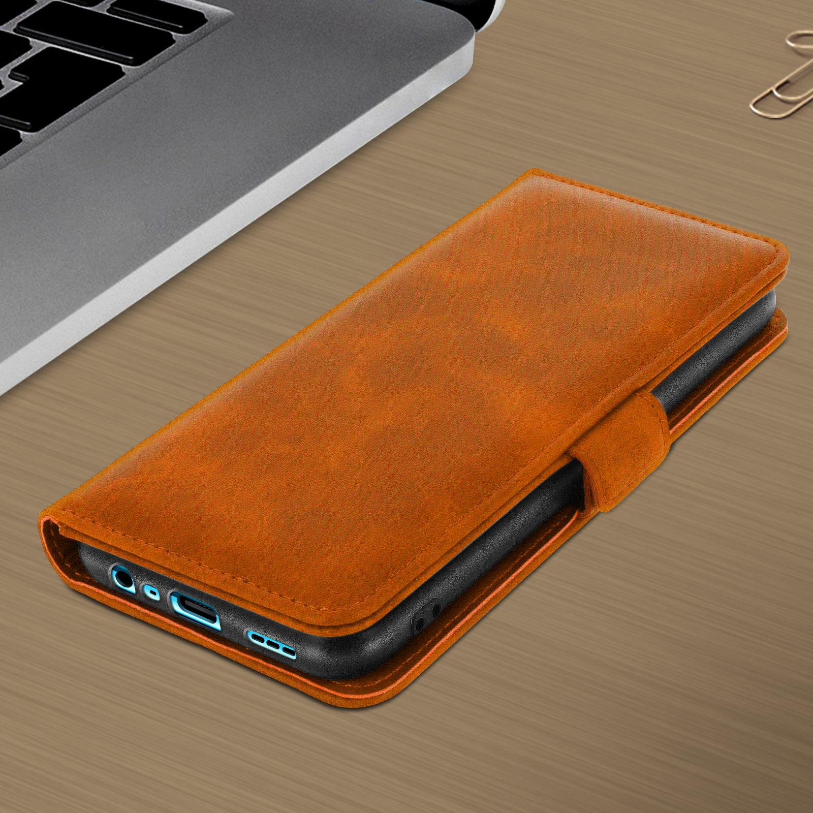 Oranje leren telefoonhoes open op een houten oppervlak. Een telefoon zit erin. Een paperclip op de achtergrond.