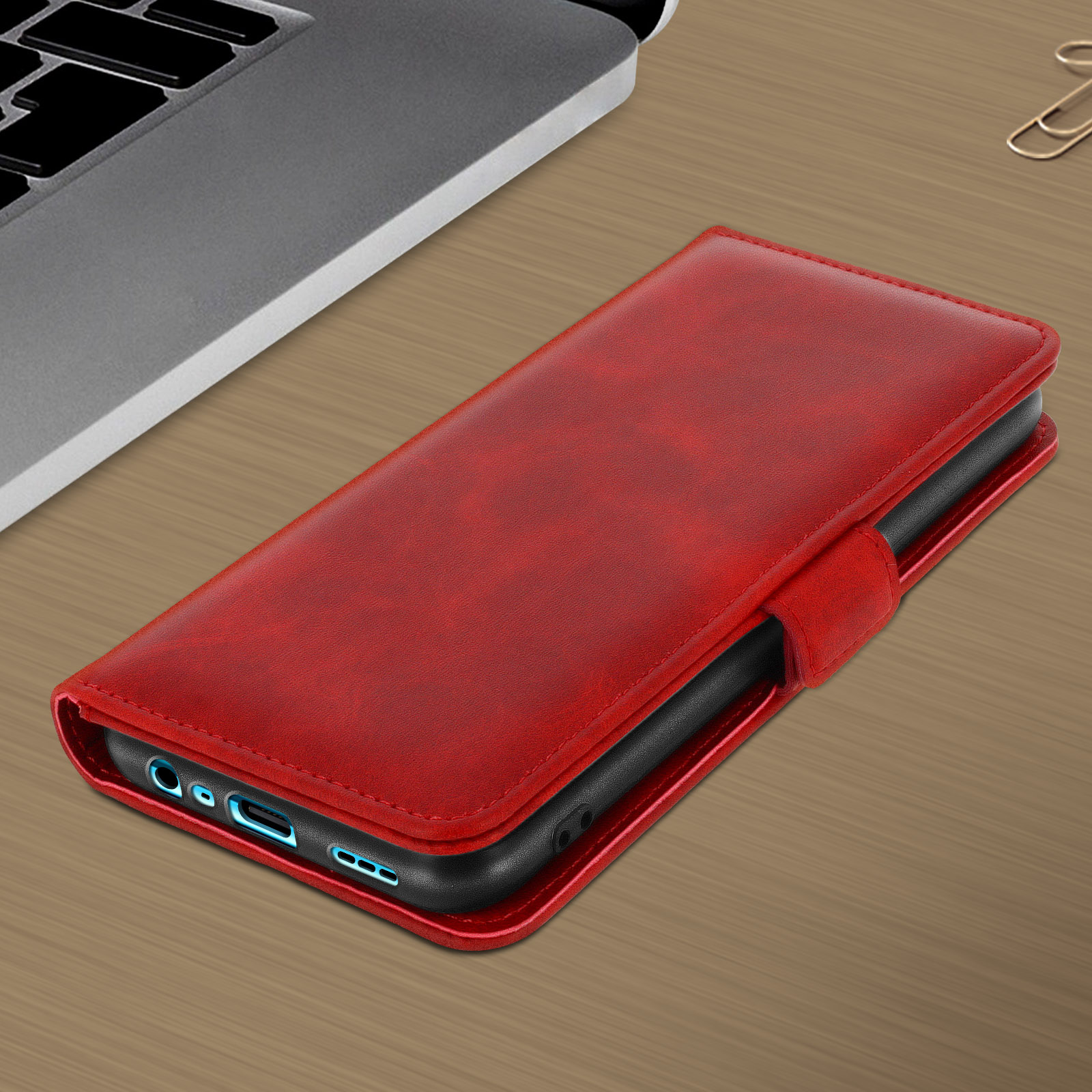 Étui de téléphone rouge fermé sur un bureau en bois, avec un ordinateur portable et d'autres objets.