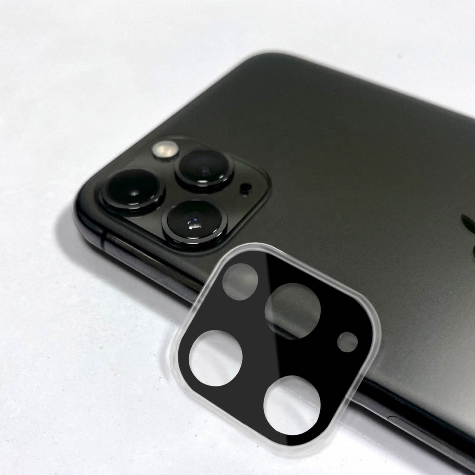 Un iPhone nero su superficie bianca. Accanto, un proteggi-obiettivo con design nero e fori trasparenti.