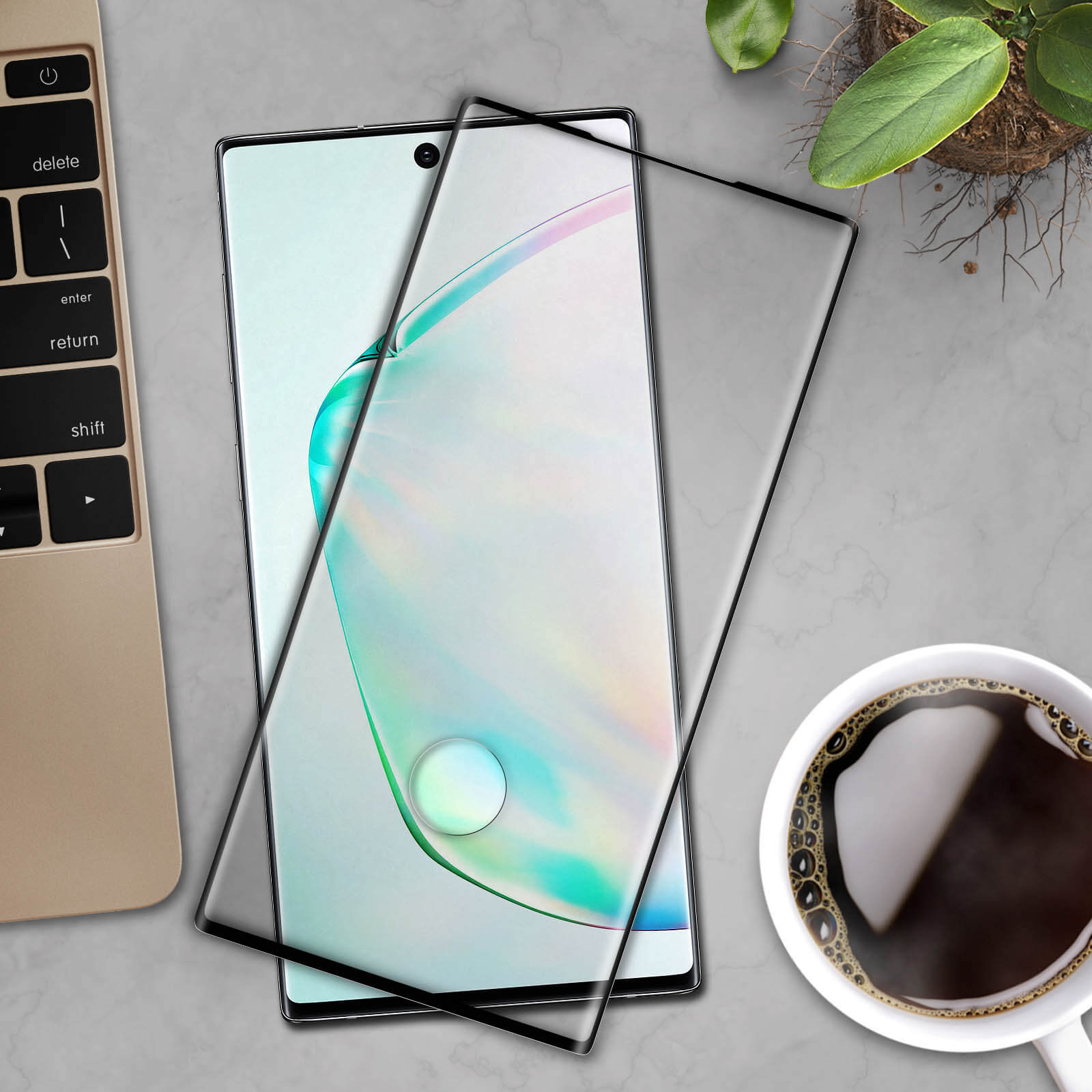 Telefoon met schermbeschermer op een bureau met toetsenbord, plant en koffiekopje.