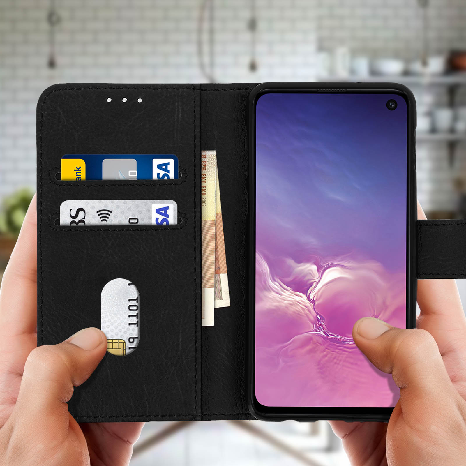 Un telefono nero in una custodia a portafoglio nera è tenuto in mano con carte e contanti visibili.
