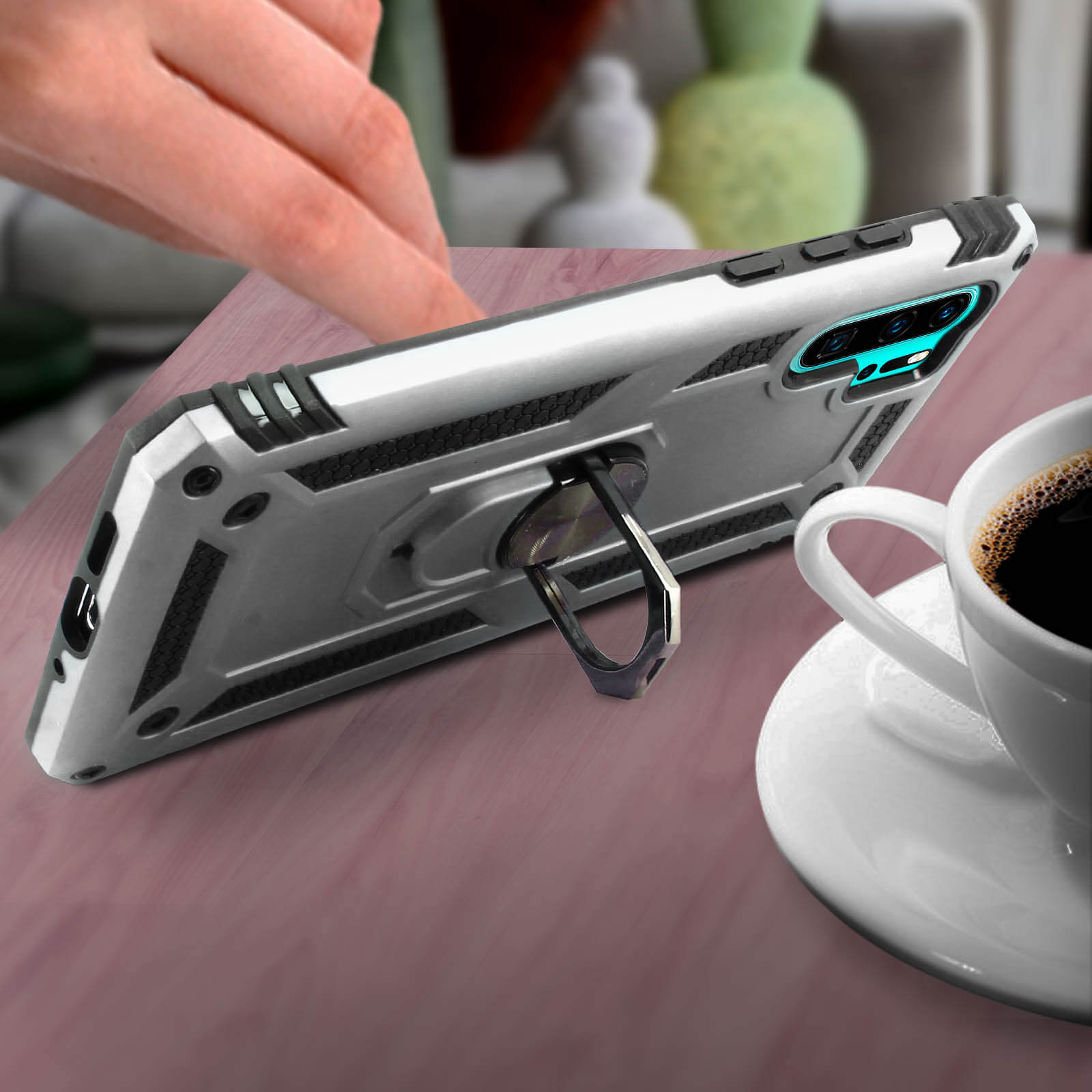 Custodia per telefono argento con anello di supporto e tazza di caffè su un tavolo. Sfondo sfocato.