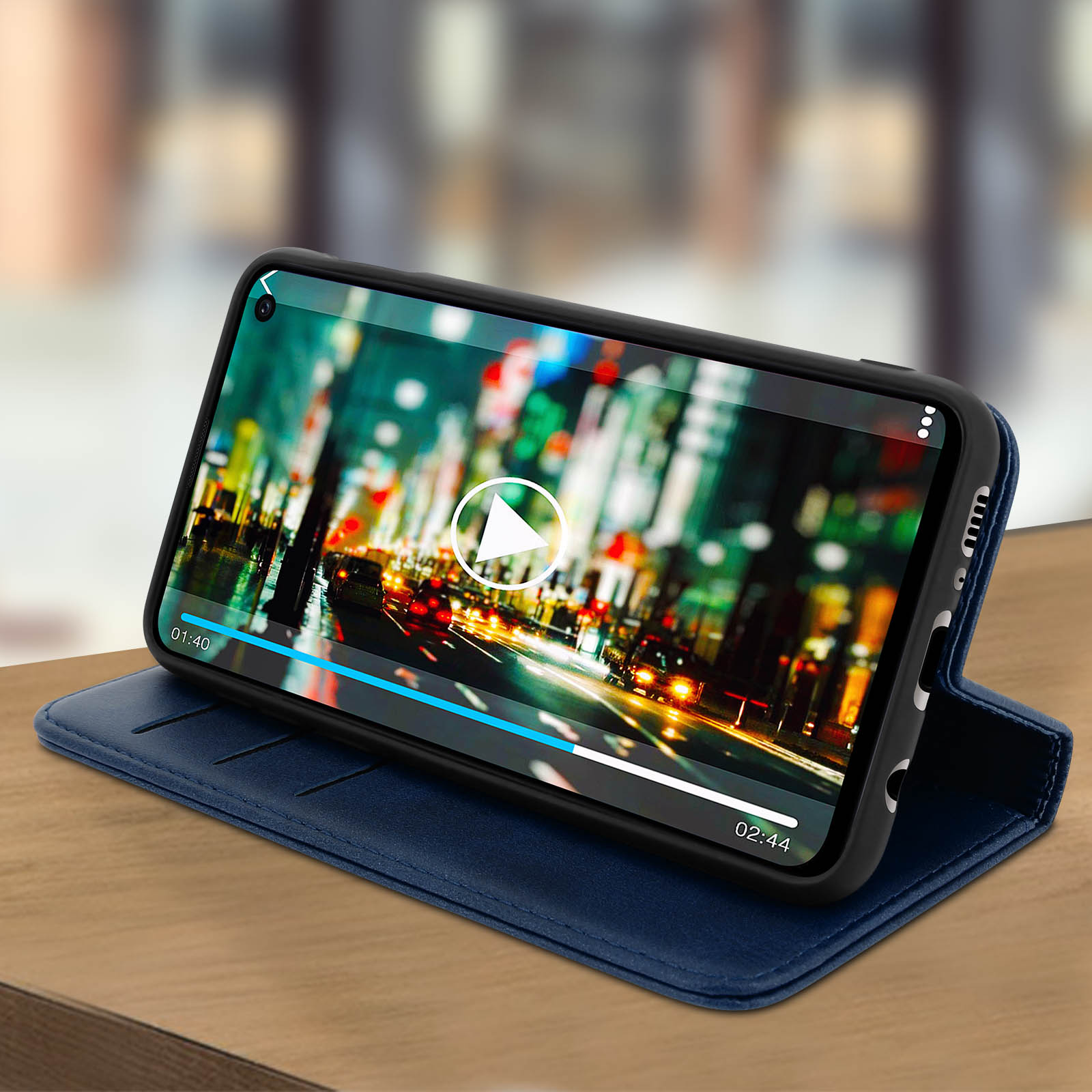Telefono in custodia blu, riproduce video di una città di notte, su superficie in legno.