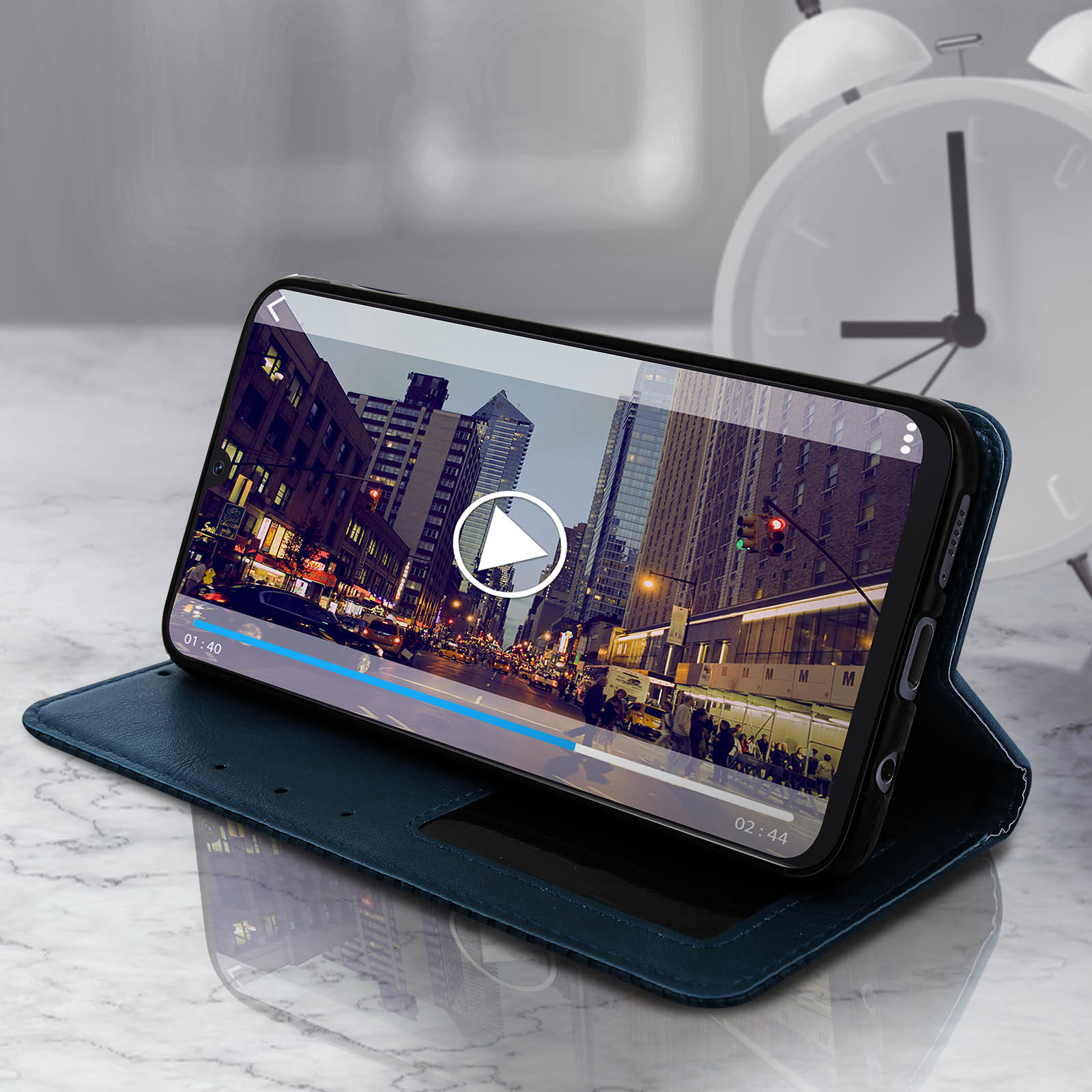 Un telefono che mostra un video su una custodia verticale, con superficie in marmo e sveglia.